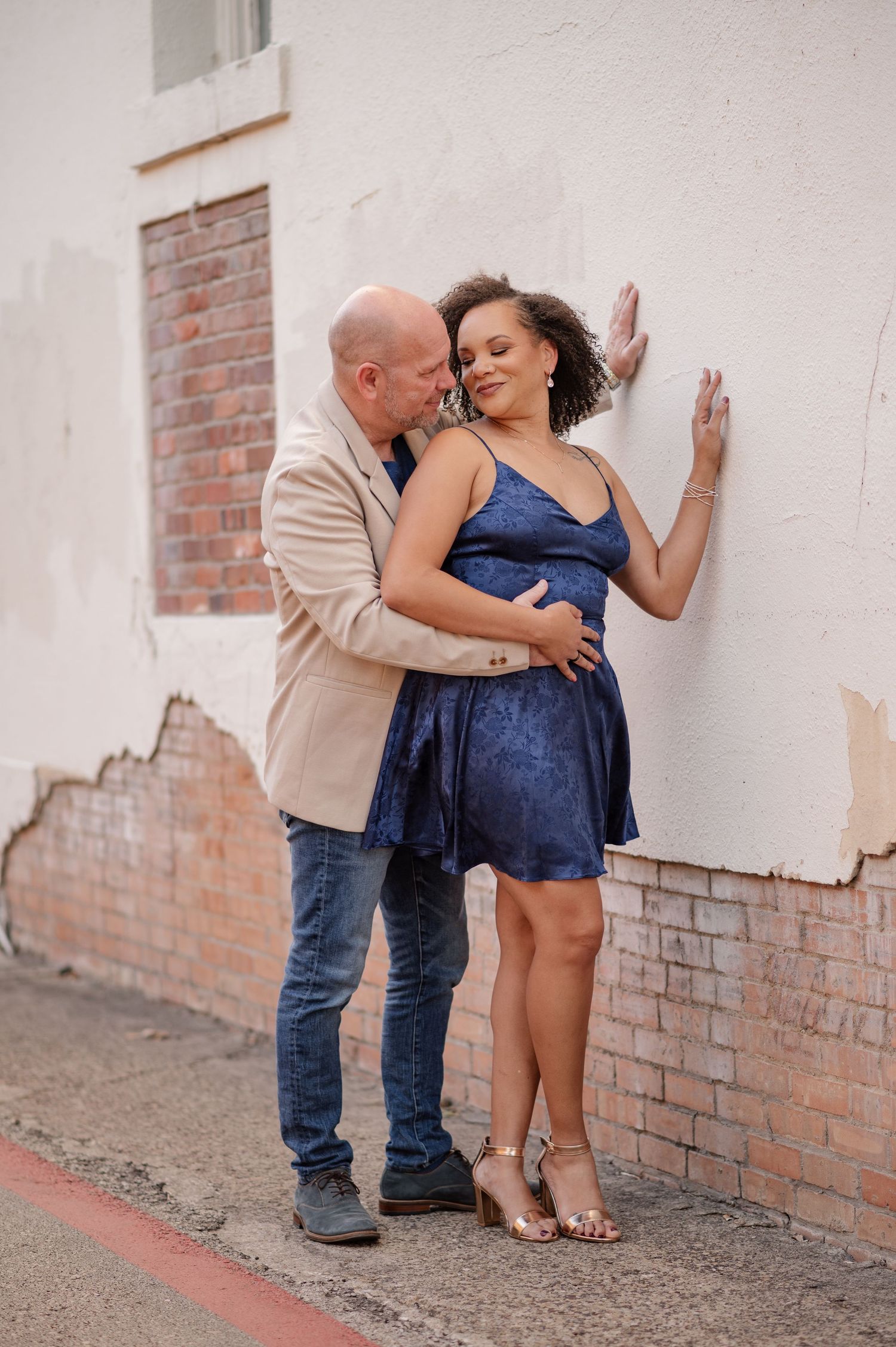 Couple intimately embracing while propped up to a brick wall in Downtown McKinney for their engagement session