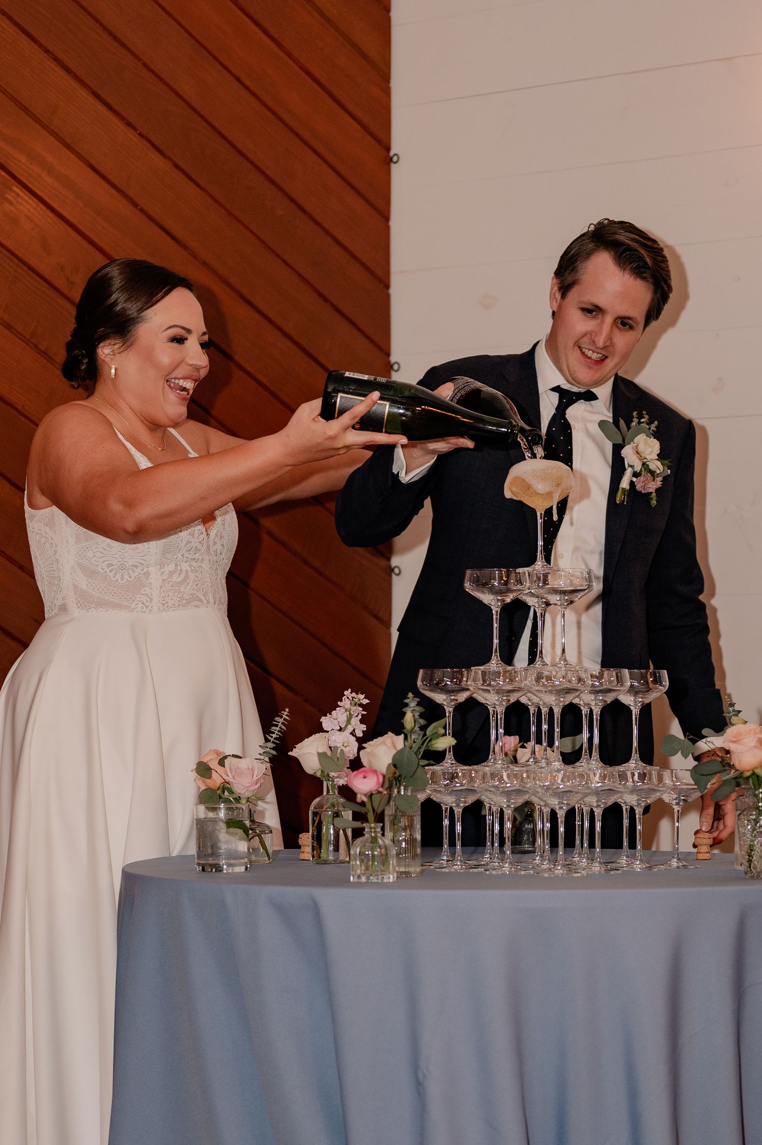 Wedding couple pouring champagne into a tower of glasses during wedding reception.