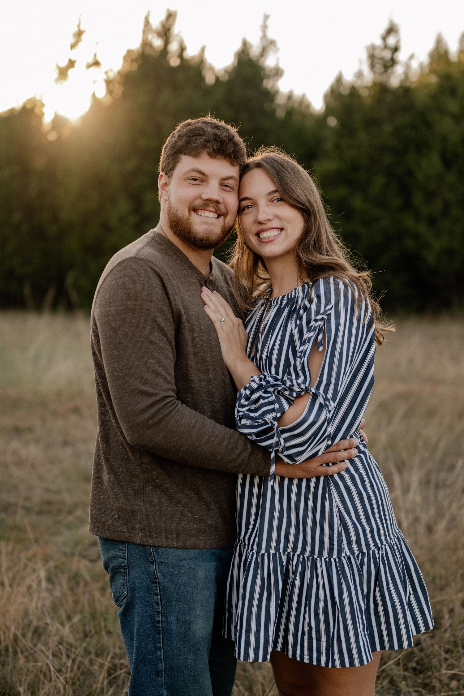 Married couple embracing during a casual fall couple session in a large tree lined field in during golden hour