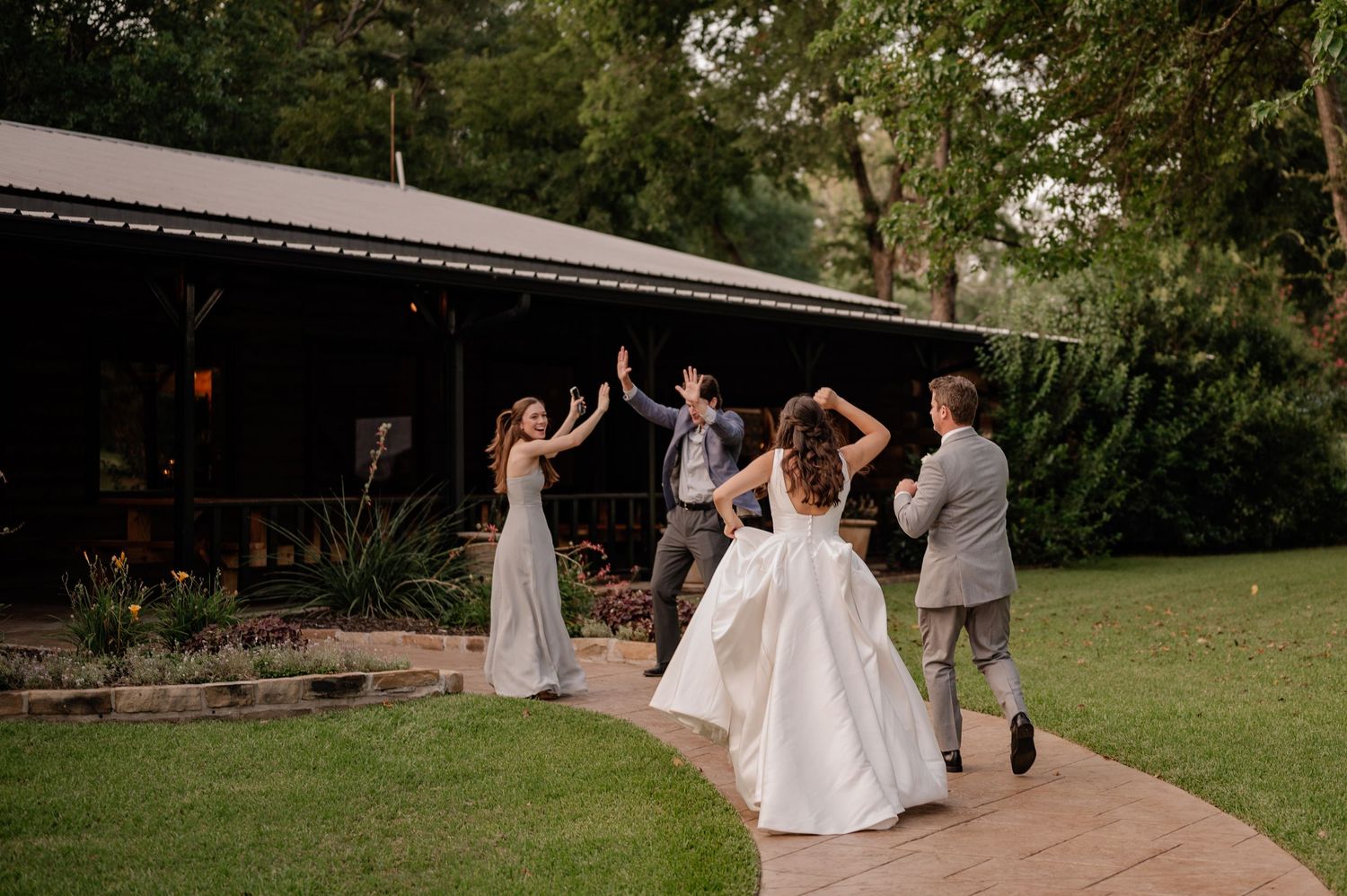 Bride and Groom candidly celebrate with two friends outside of the wedding reception hall surrounded by Spring greenery in Plano, Texas