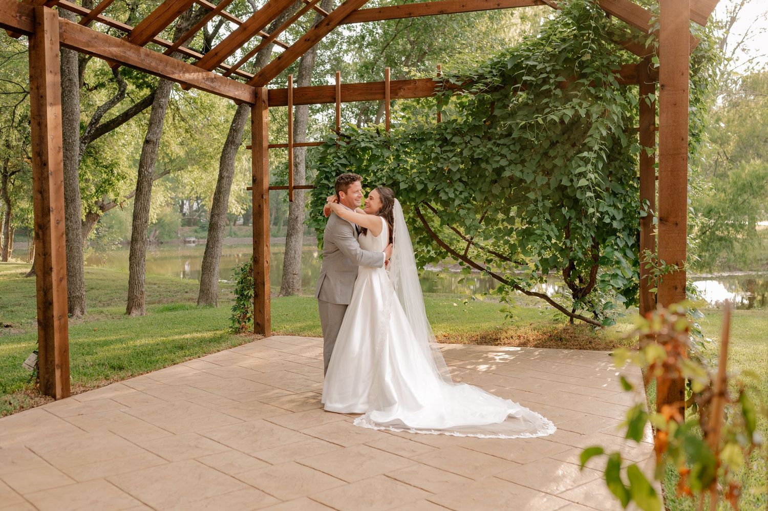 Bride & groom under a covered outdoor walkway surrounded by lush greenery in a garden setting in Plano, TX during wedding couple portraits