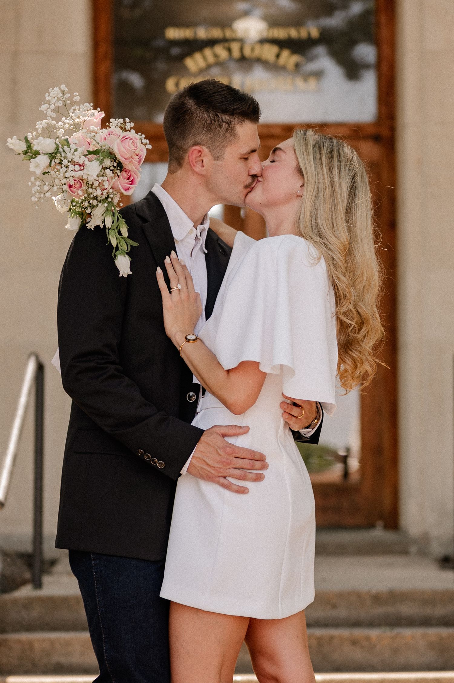Married couple embracing and kissing outside of downtown Rockwall courthouse during elopement wedding photo session