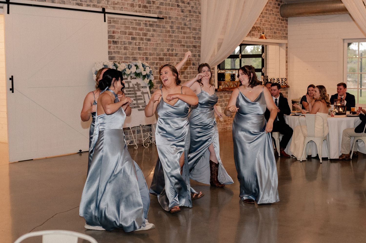 Bridesmaids in blue silk dresses entering the reception hall while energetically dancing and laughing