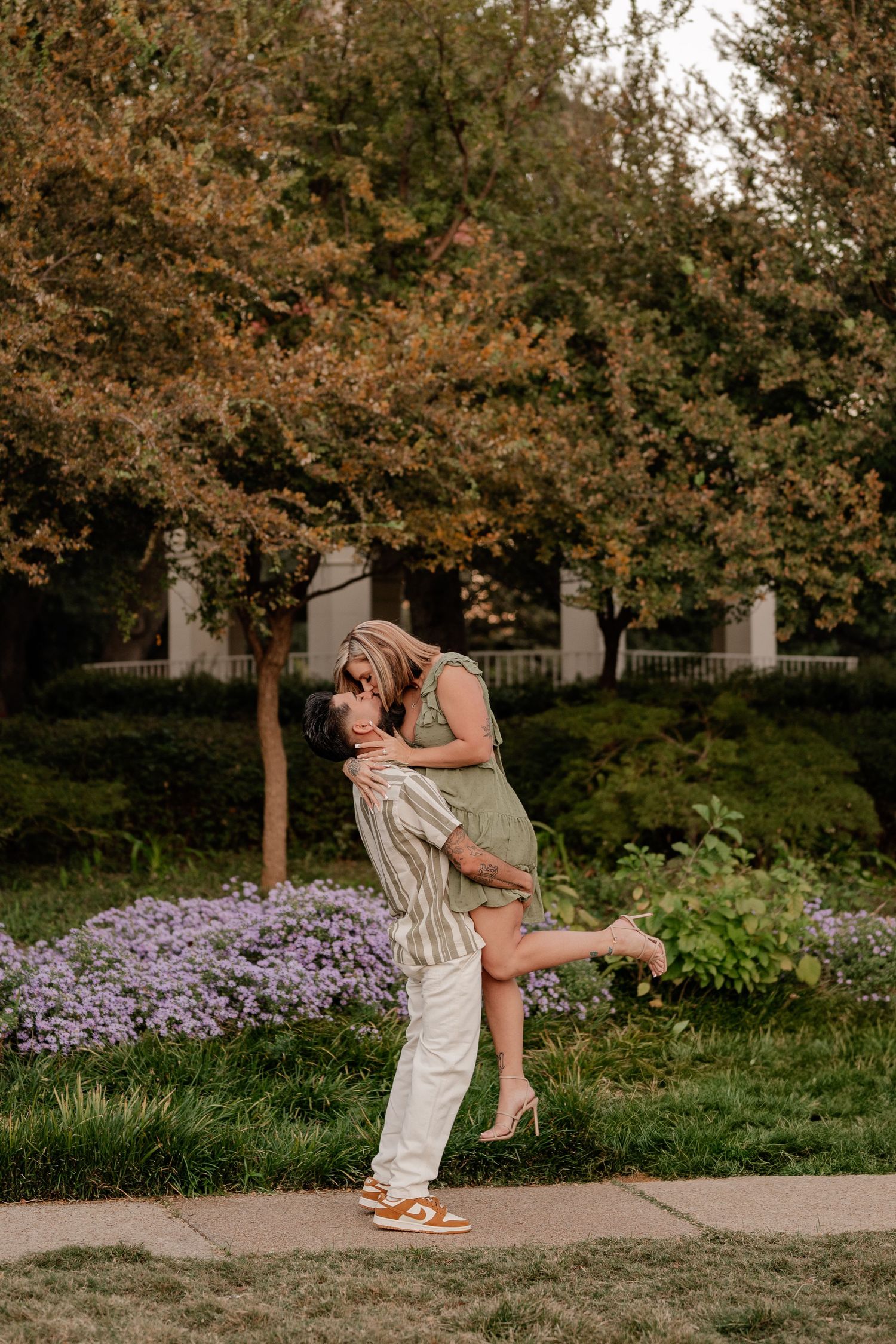Couple kissing in front of the greenery and floral lined gazebo at Flippen Park in Dallas for their summer engagement photo session