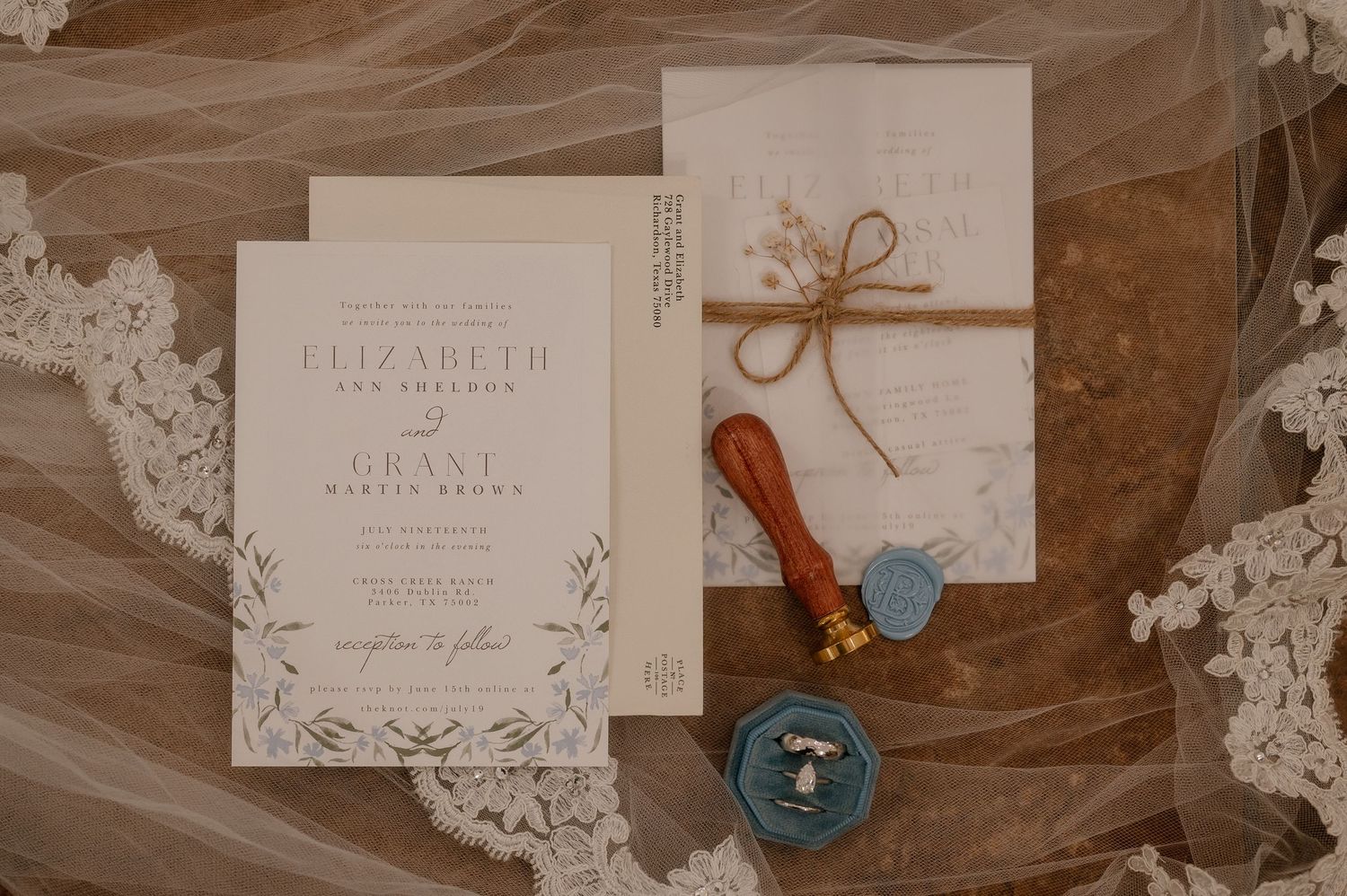 Wedding stationary on the floor with a ring box, wedding rings, and a custom wax seal