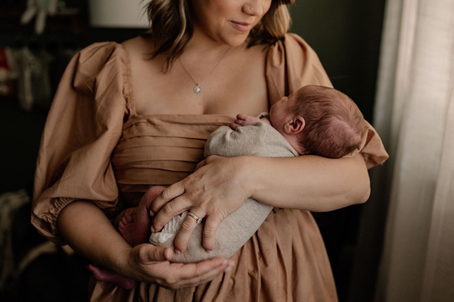 Intimate close up of a mom holding her newborn baby near natural light at an at-home newborn photo session in Dallas, Texas