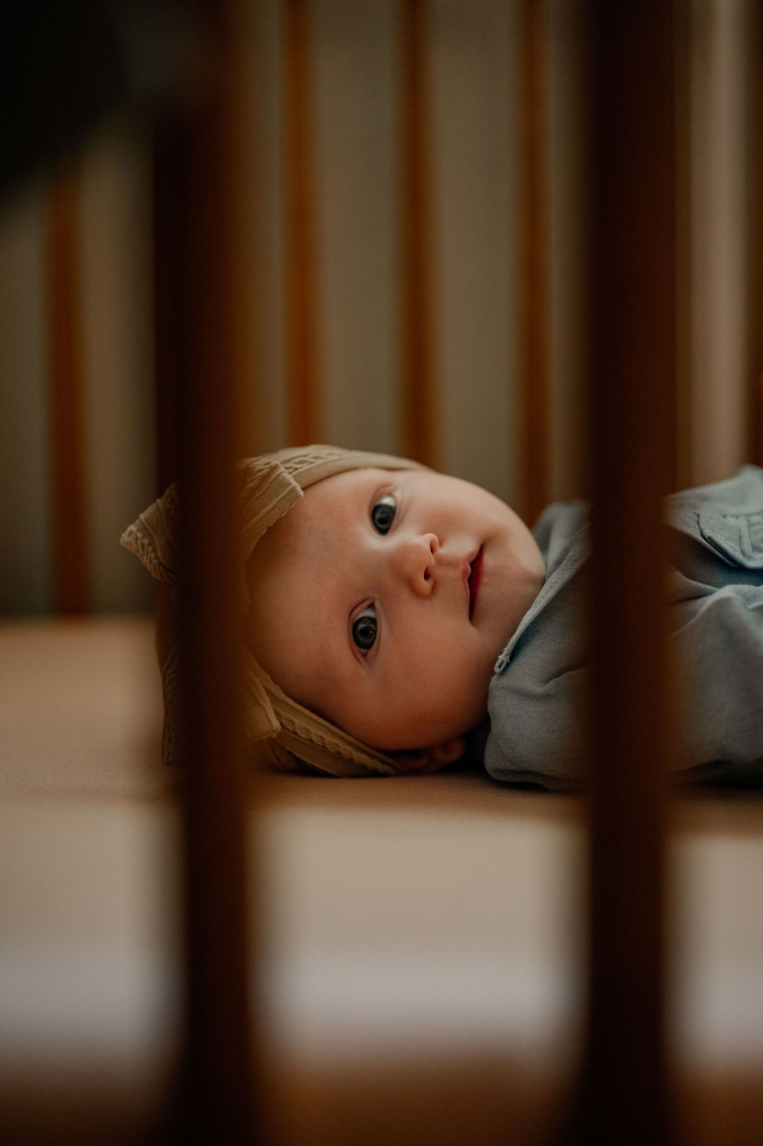 View through crib slats of baby lying in nursery crib.