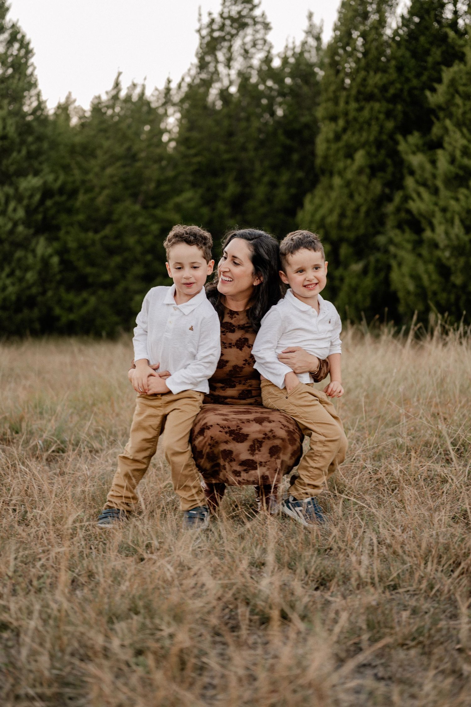Mother embracing her sons in a large field lined with trees at an outdoor family session for fall photos in Sunnyvale, Texas