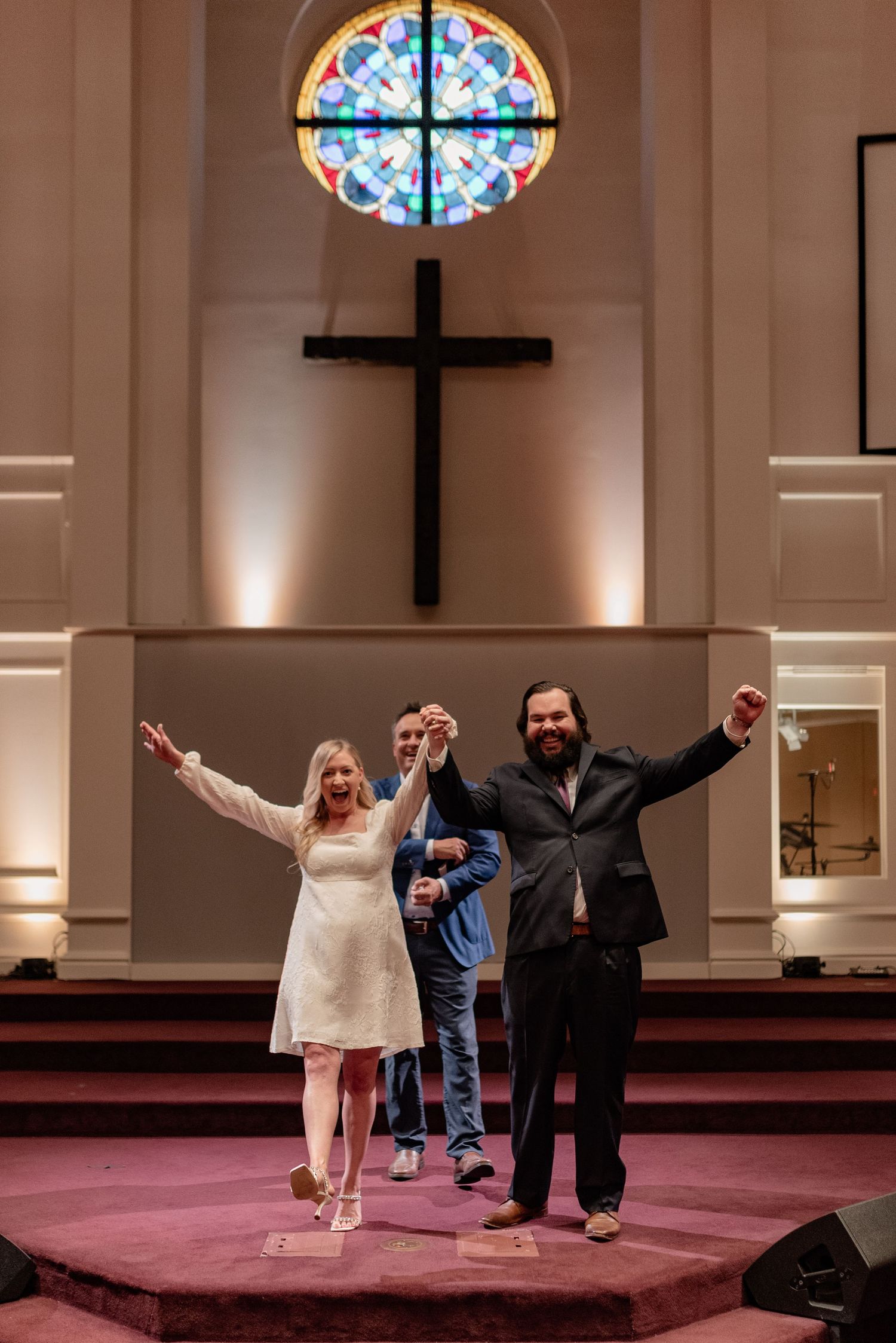 Joyful celebration moment inside a church sanctuary with stained glass window and cross.