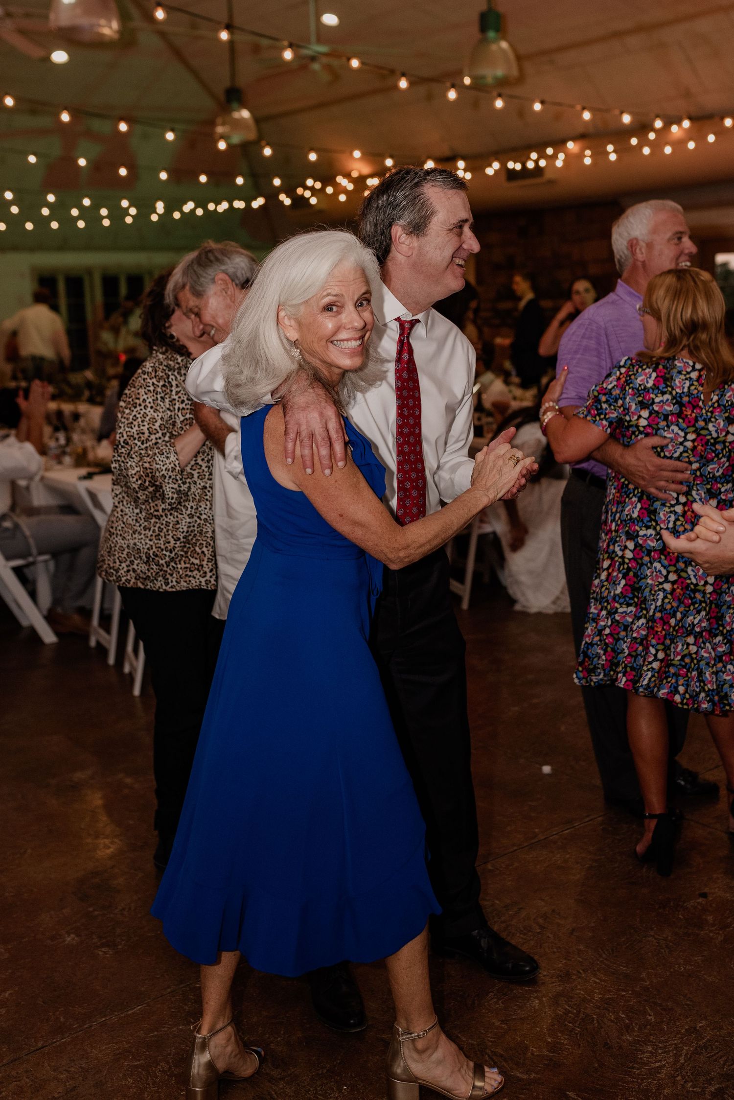 Couples dancing together at wedding reception under string lights.