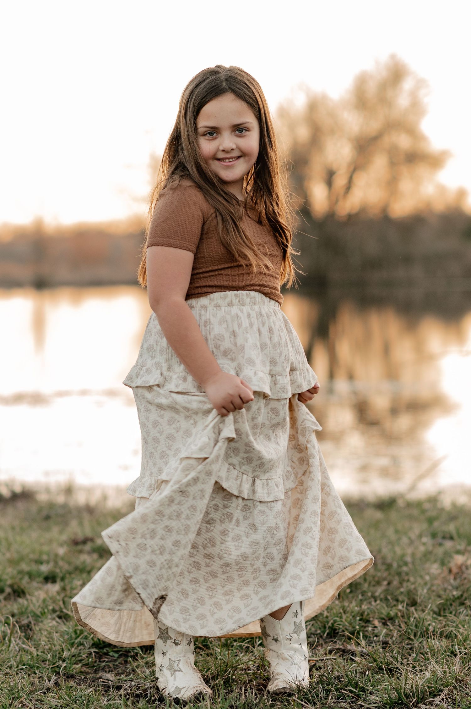 Candid photo of a joyful young girl at an at-home family session in front of a large pond on their farm in Greenville, TX