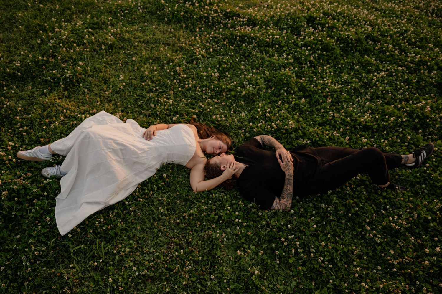 Wide shot of a couple laying in nice clothes in a clover field during a summer engagement photo session in East Dallas, Texas