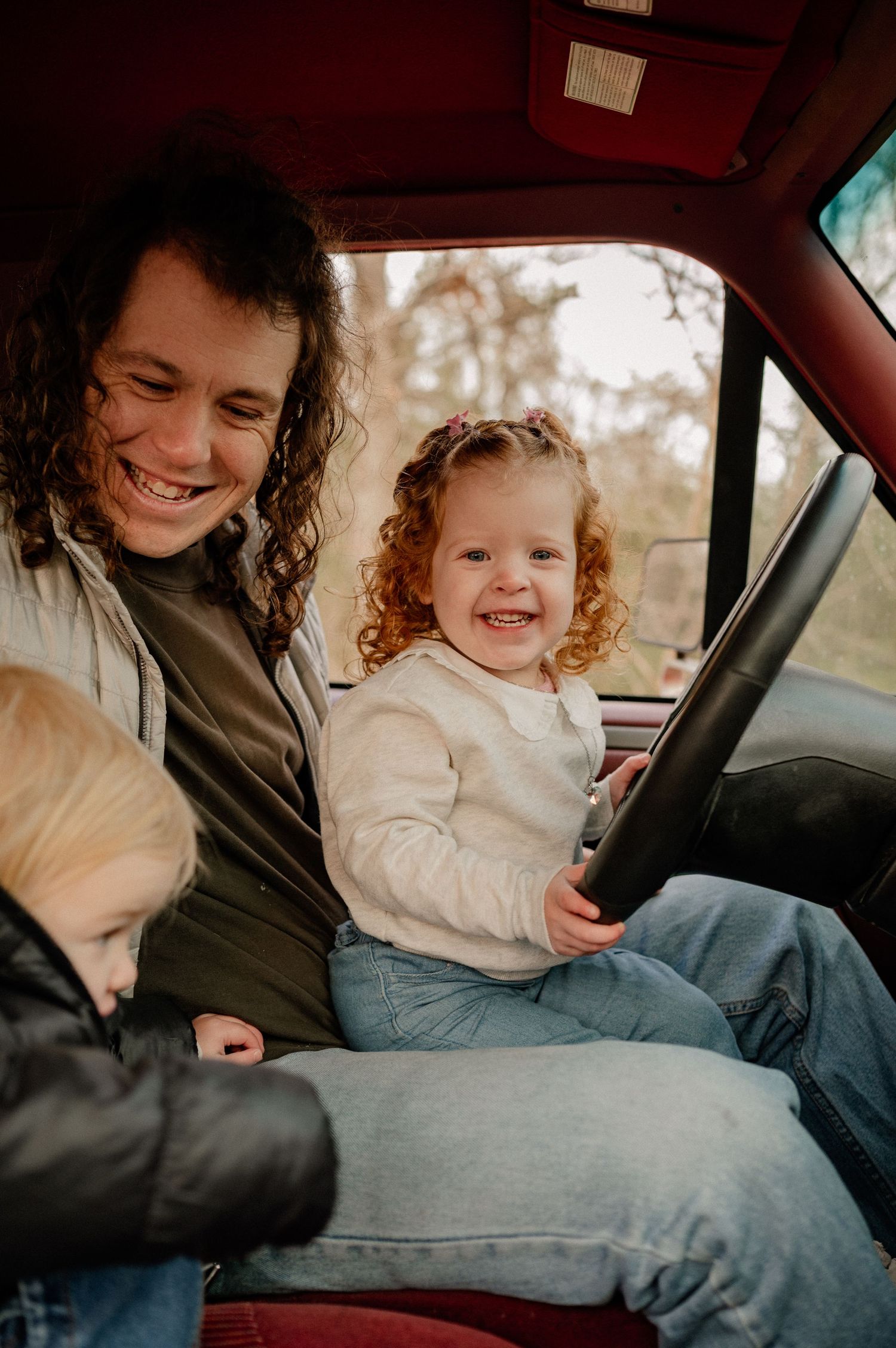 Father and kids candidly playing and laughing in the cab of a red vintage truck for a winter family photo session