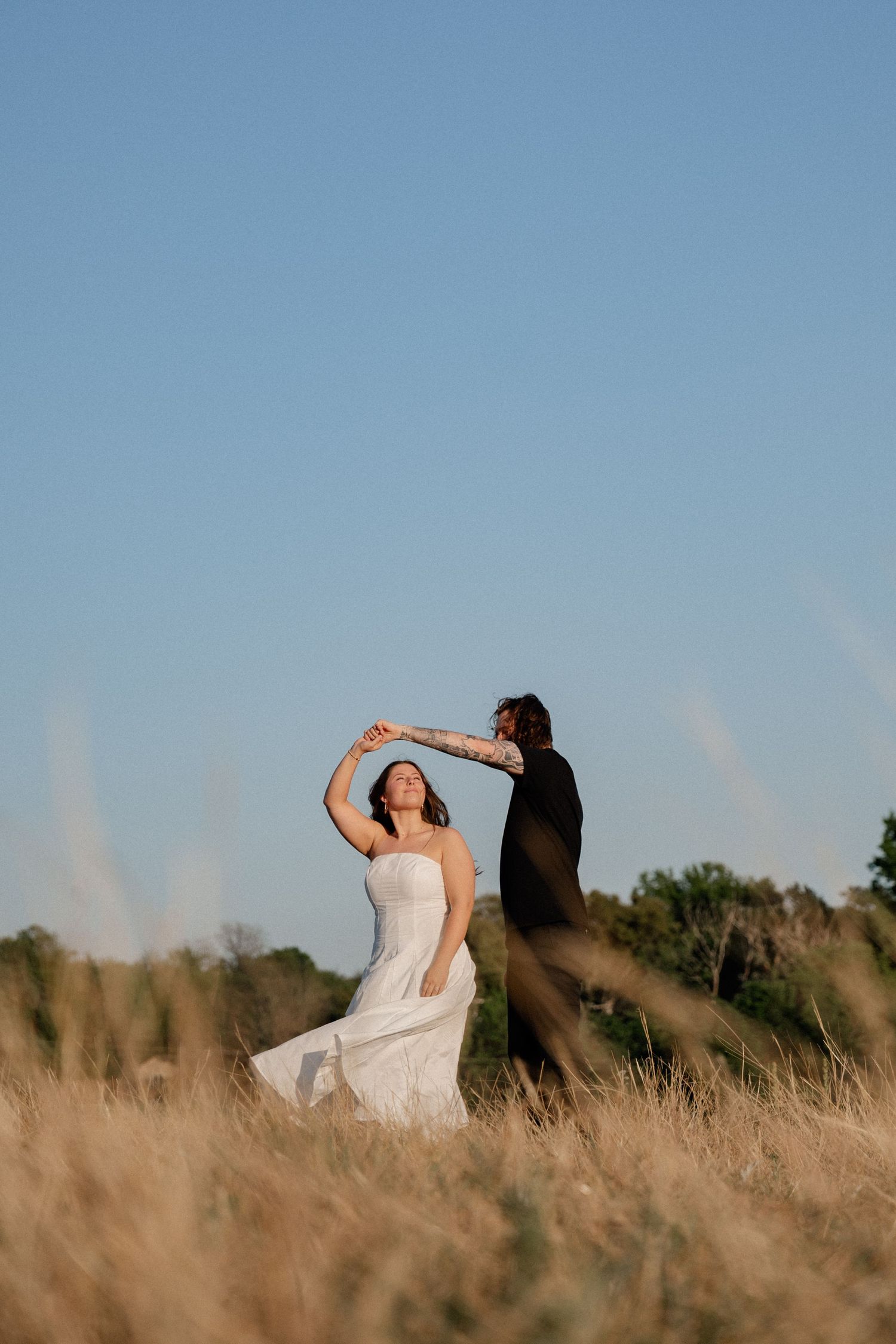 A couple dances during their engagement photo session in a golden field under a clear blue sky in Dallas, Texas