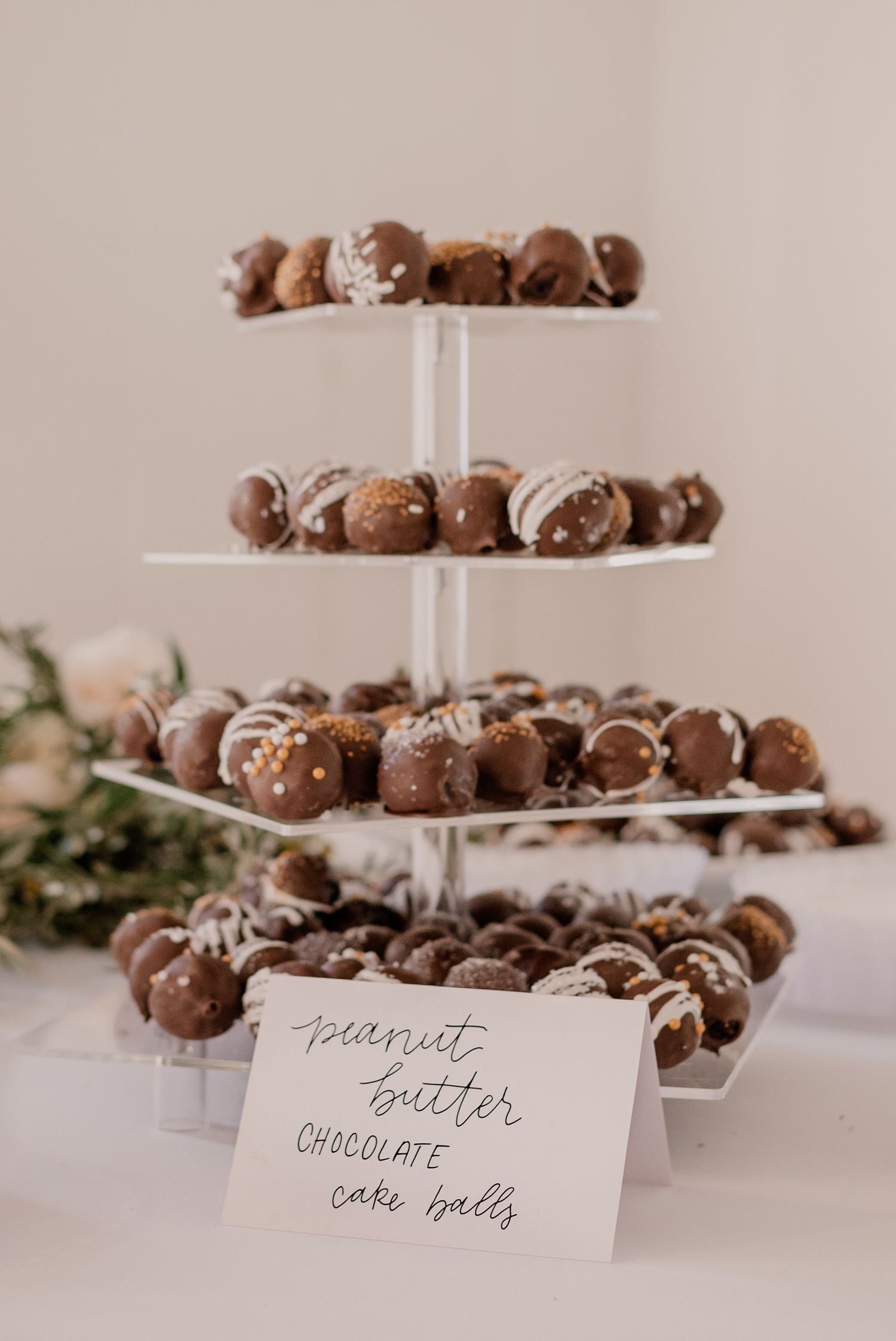 Tiered display of chocolate cake pops with handwritten label at dessert table.