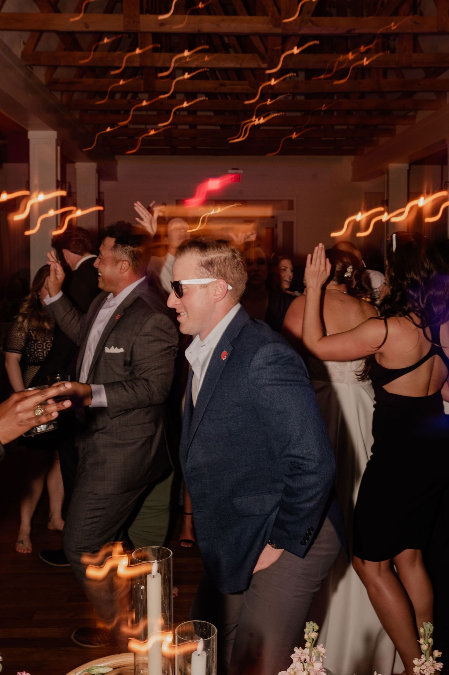 Wedding guests dancing under warm lighting with light trails creating a festive atmosphere.