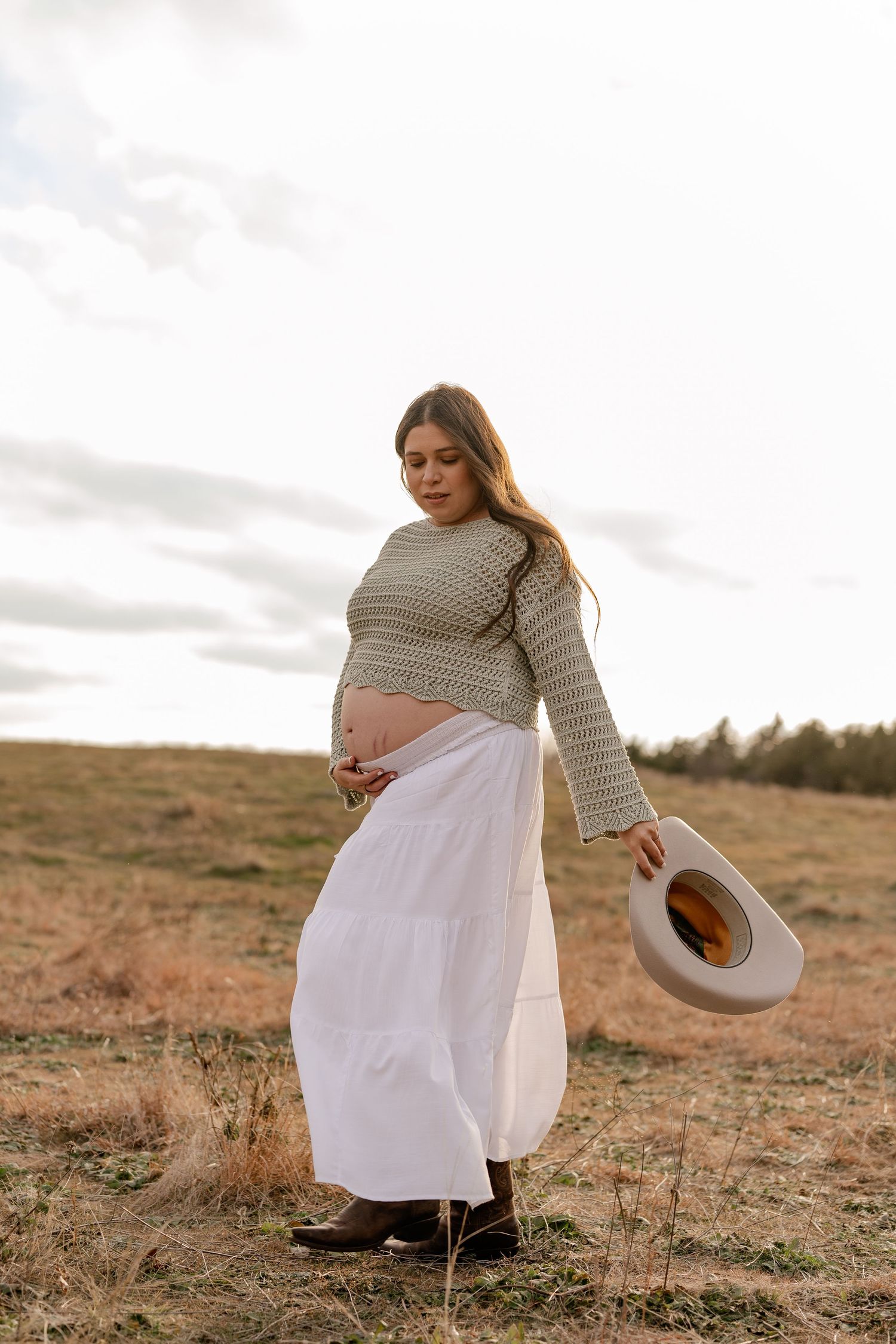 Candid photo of pregnant woman walking through wide grassy field in western outfit for a maternity session in Plano, Texas
