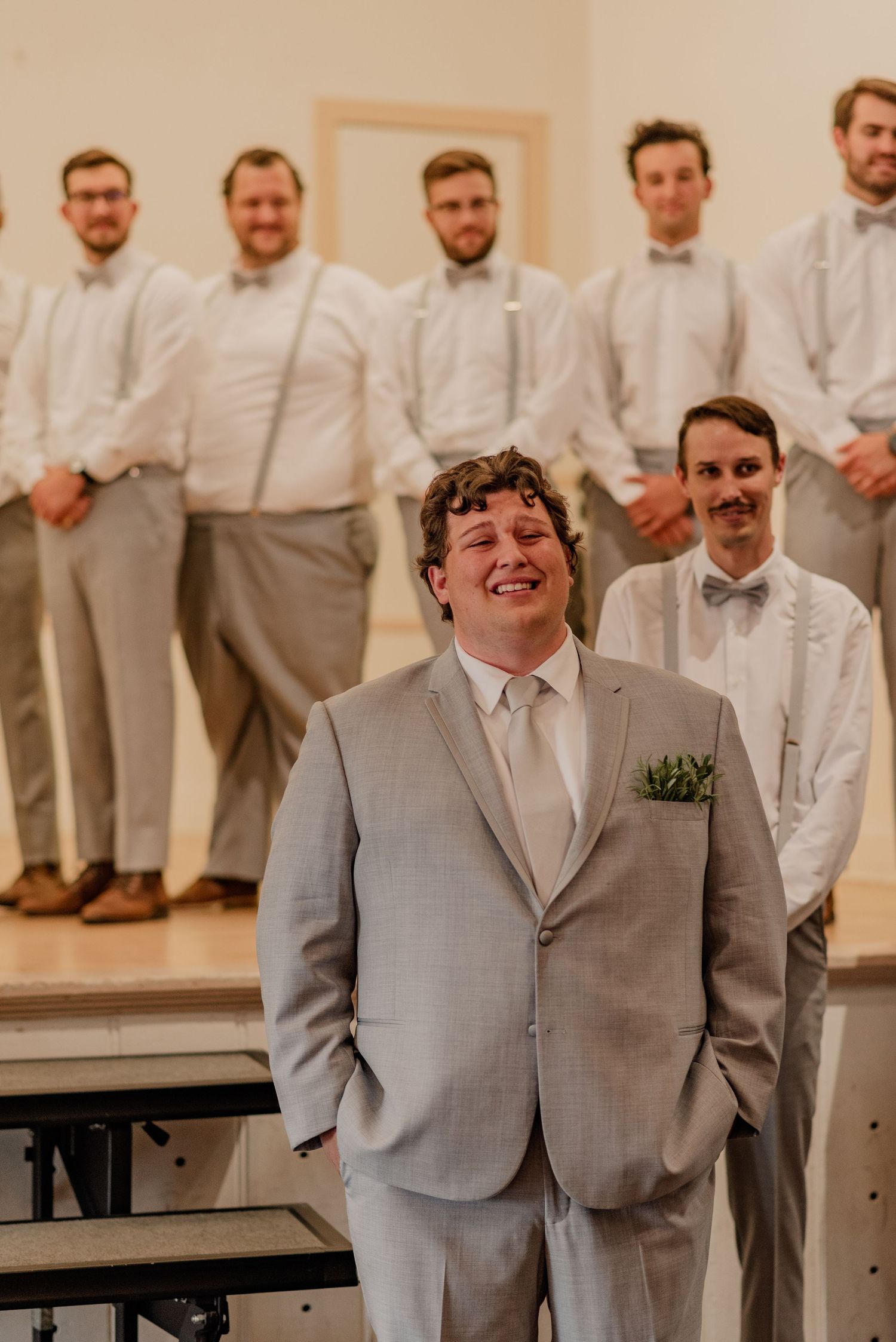 Groomsmen in matching light gray suits and white shirts stand together indoors.