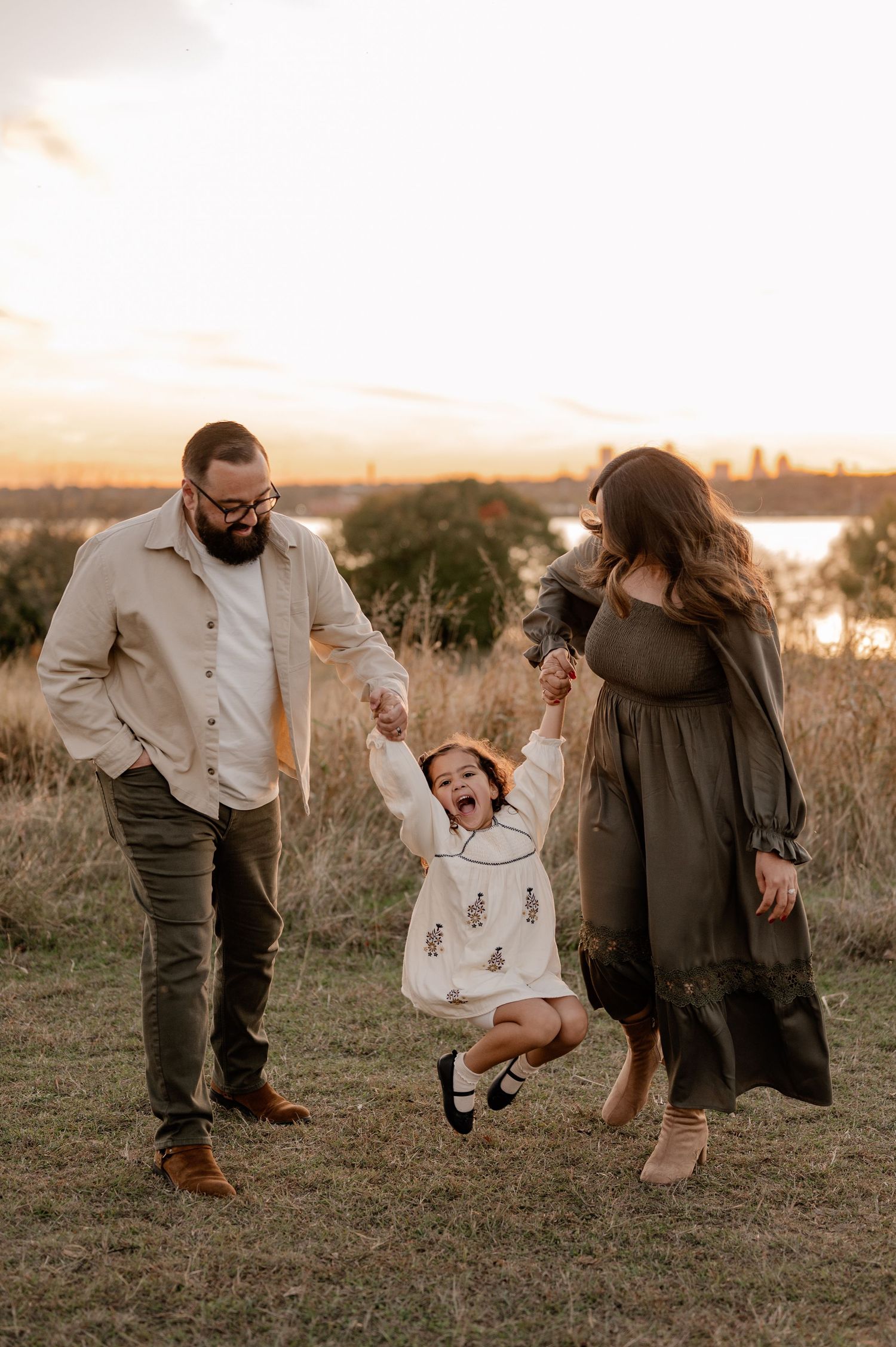 Candid photo of family joyfully swinging daughter overlooking the White Rock Lake in East Dallas, Texas