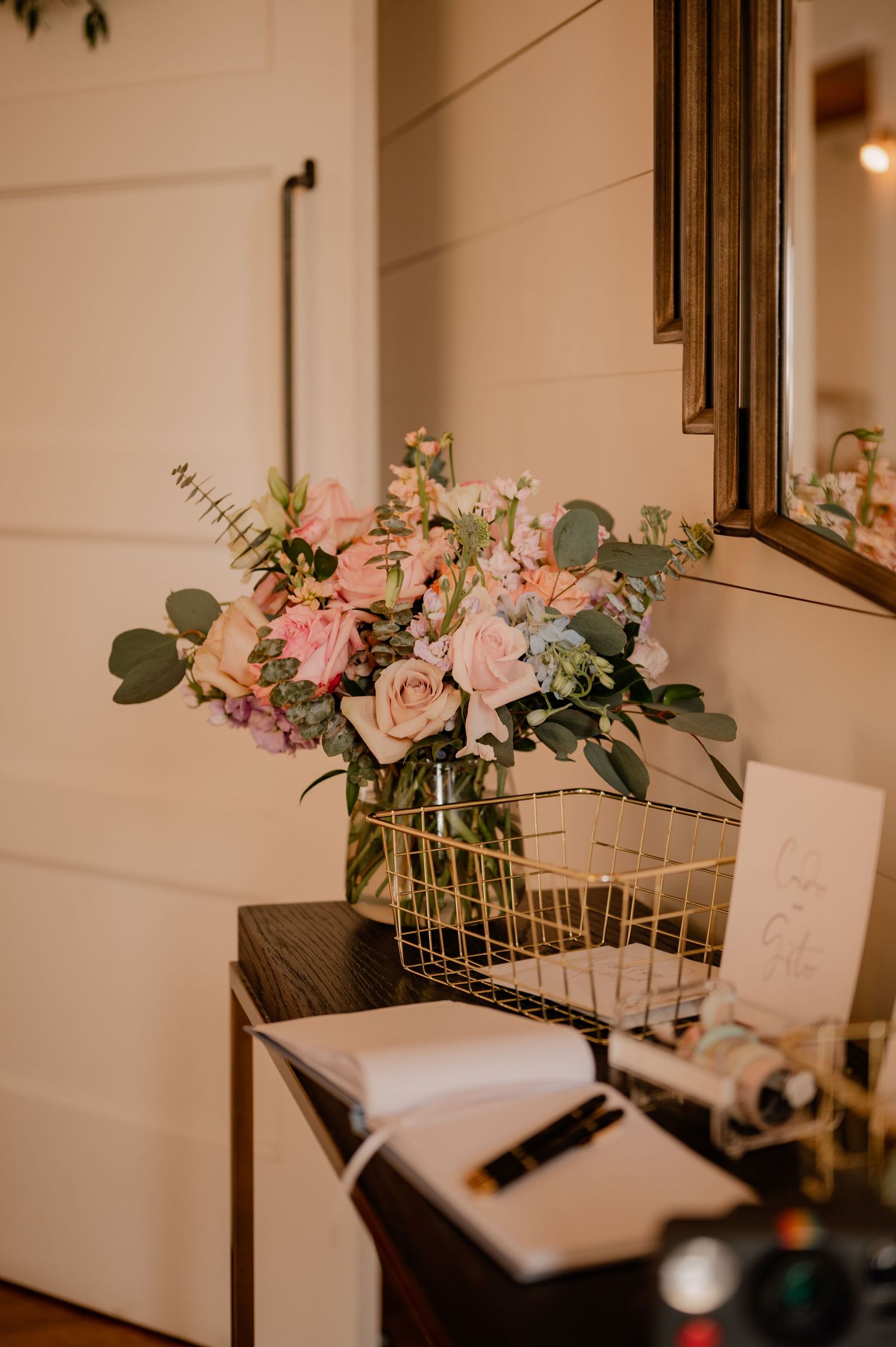 Pink and white floral arrangement with eucalyptus in glass vase next to vintage camera.