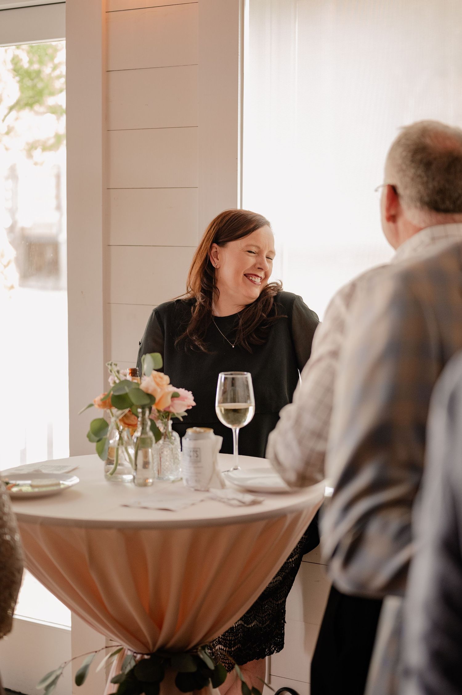 Casual cocktail wedding reception with guests chatting at high top table with wine glasses.