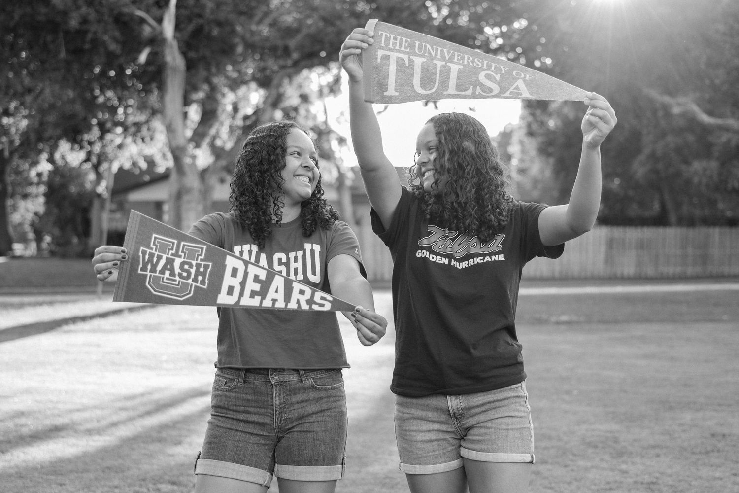 Black and white photo of Senior twins holding their college pennants in a large park at golden hour in Richardson, Texas