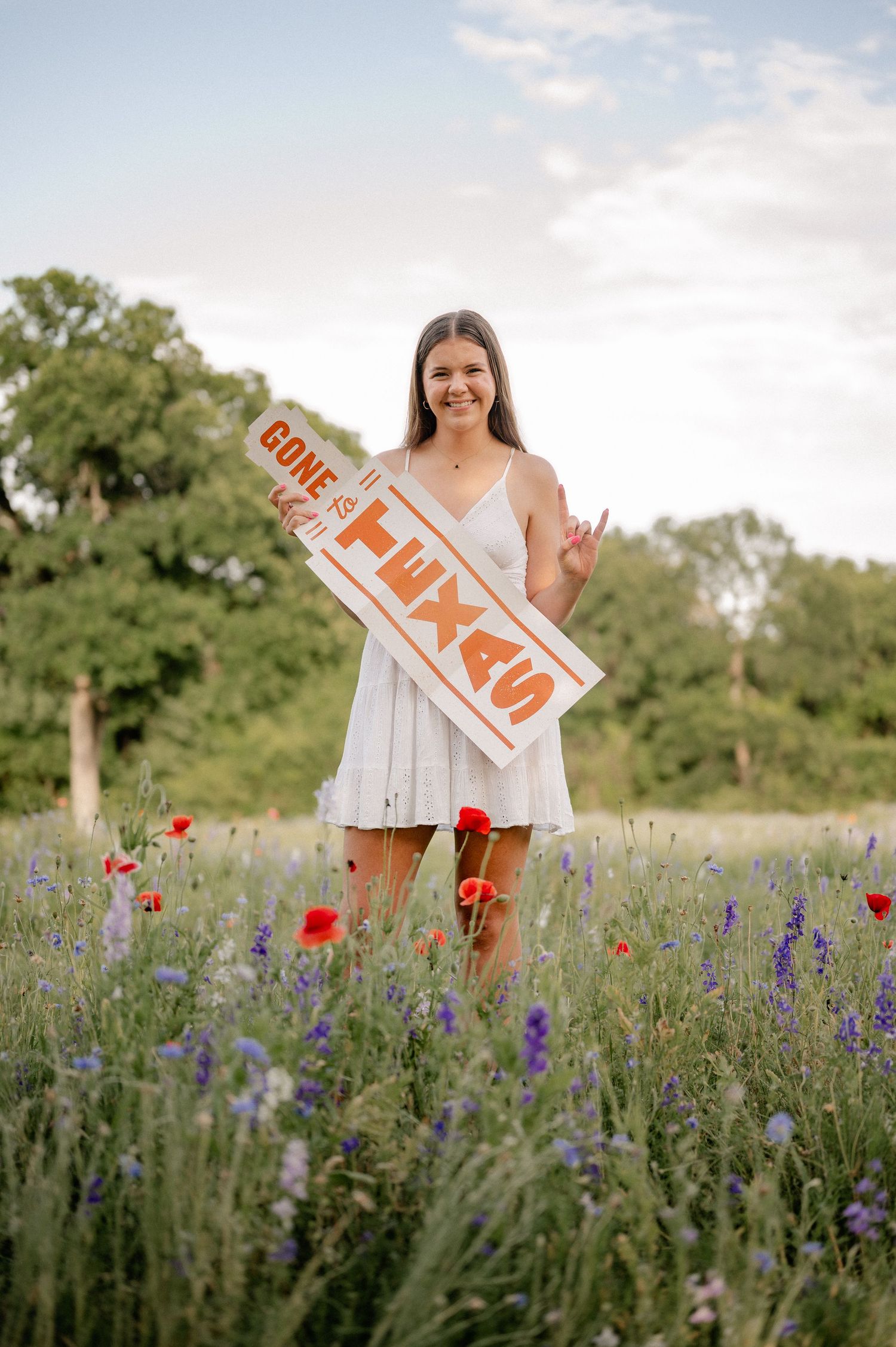 Girl posing with University of Texas acceptance sign in a field of wildflowers in Richardson, Texas for a summer senior photo session