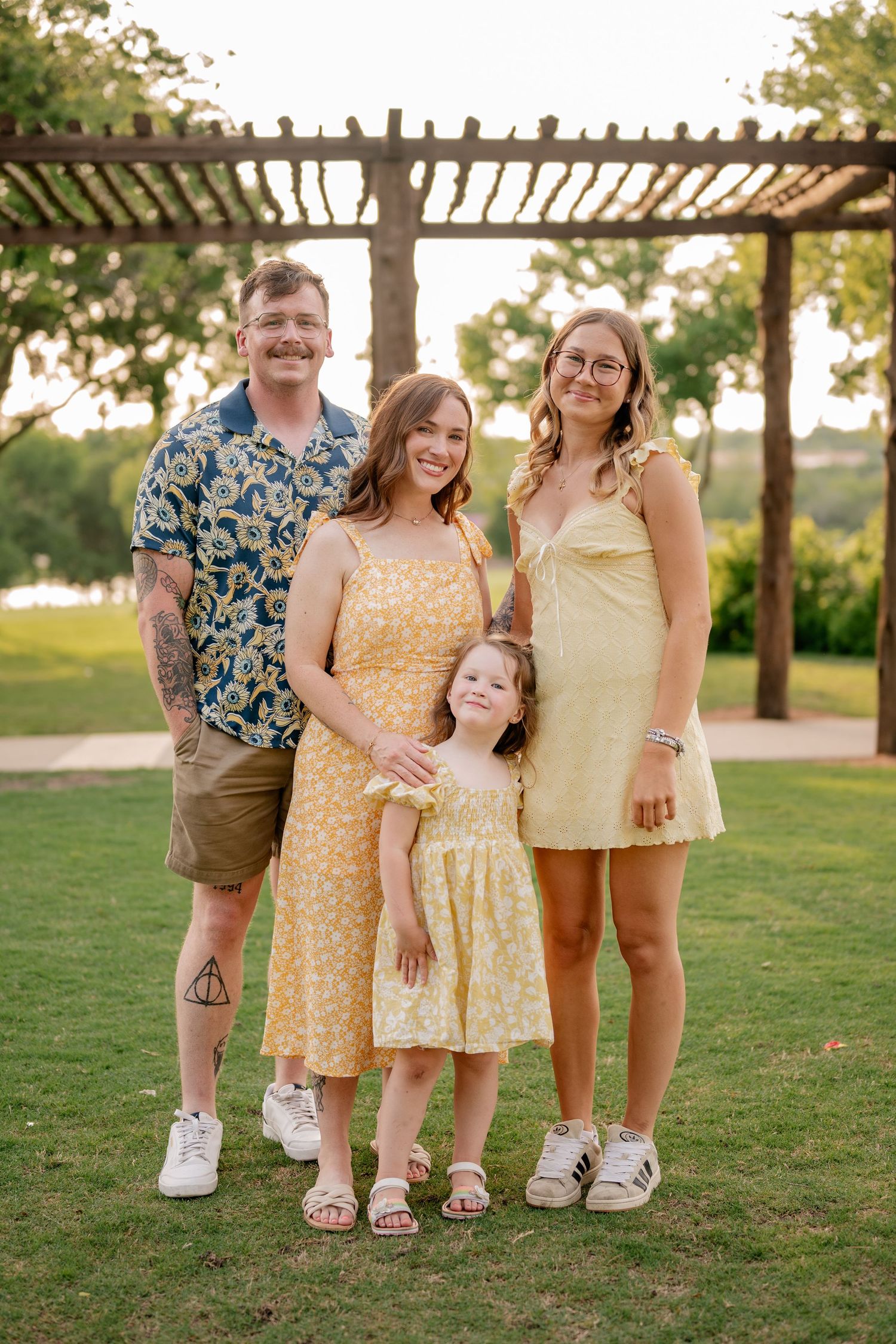Family of four posing for Spring family photos in vivid colors at large tree lined park in Rockwall, Texas