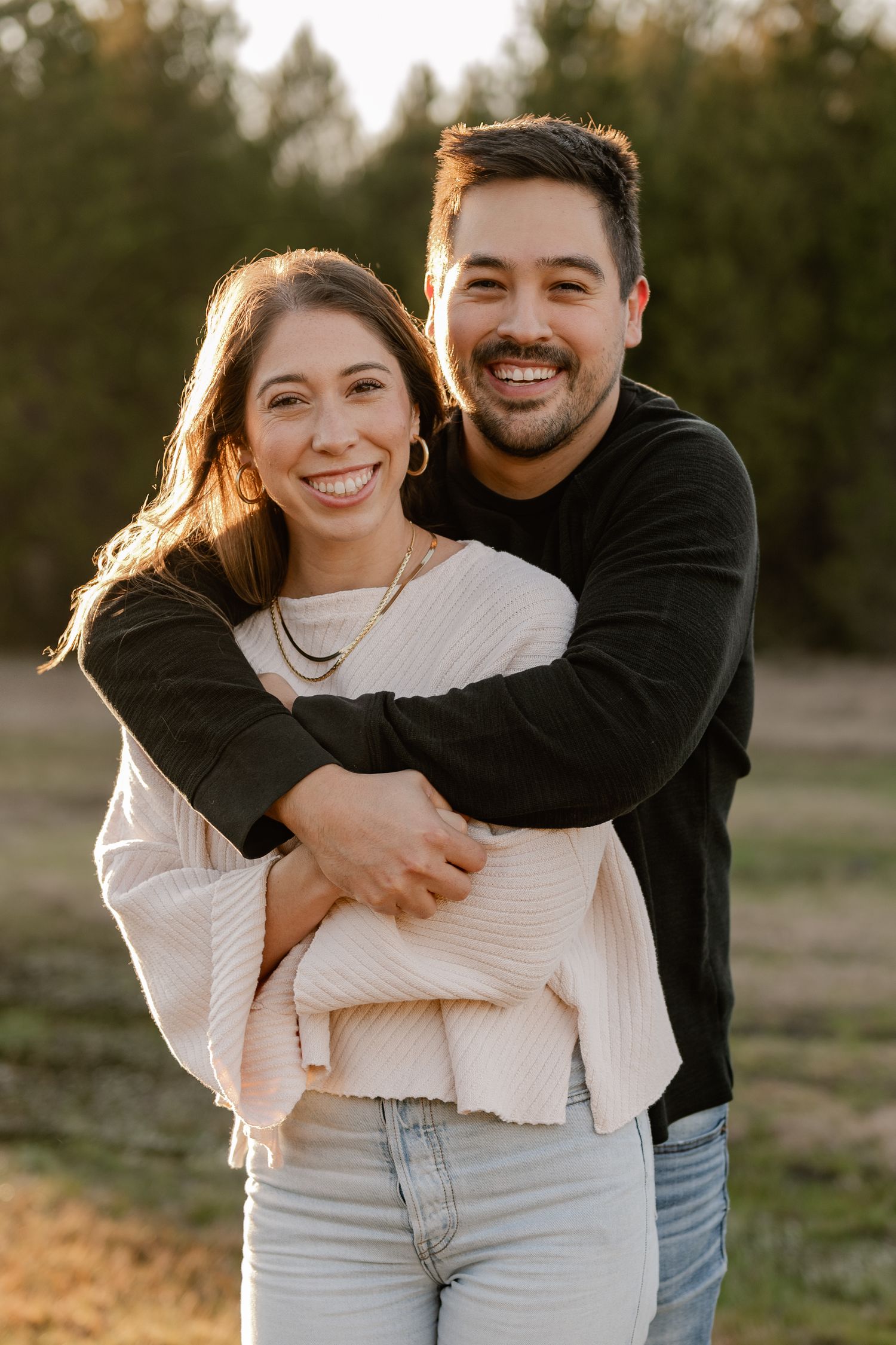 Joyful posed photo of husband bear hugging wife at a couple's photo session in a large tree lined field in Sunnyvale, Texas