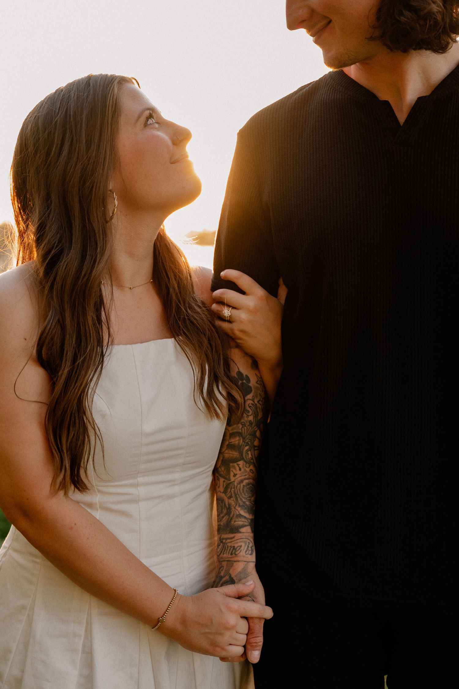 Intimate photo of couple embracing while girl looks up at her fiance with a sunset over White Rock Lake in the background.