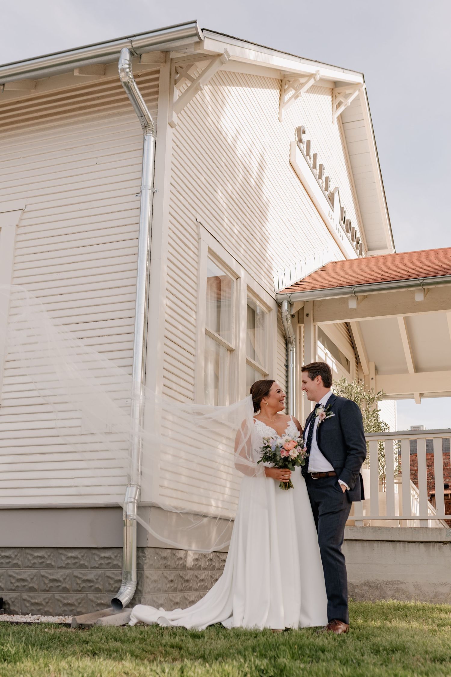 Newlyweds intimately embrace outside a Bishop Arts venue in Dallas, Texas while bride's veil blows in the wind