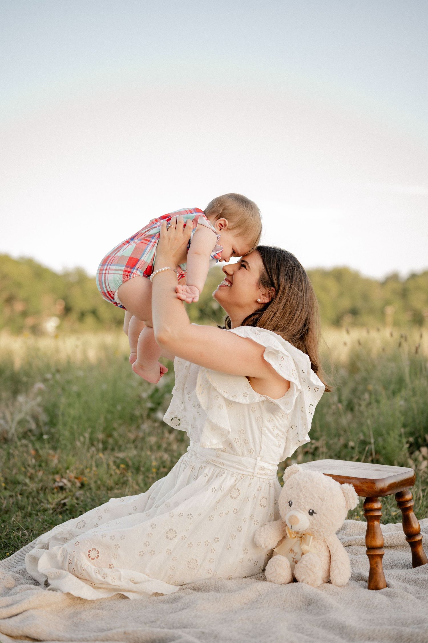 Candid of Mother playing with her baby over her head while sitting on a blanket in a large open field for a Dallas family session