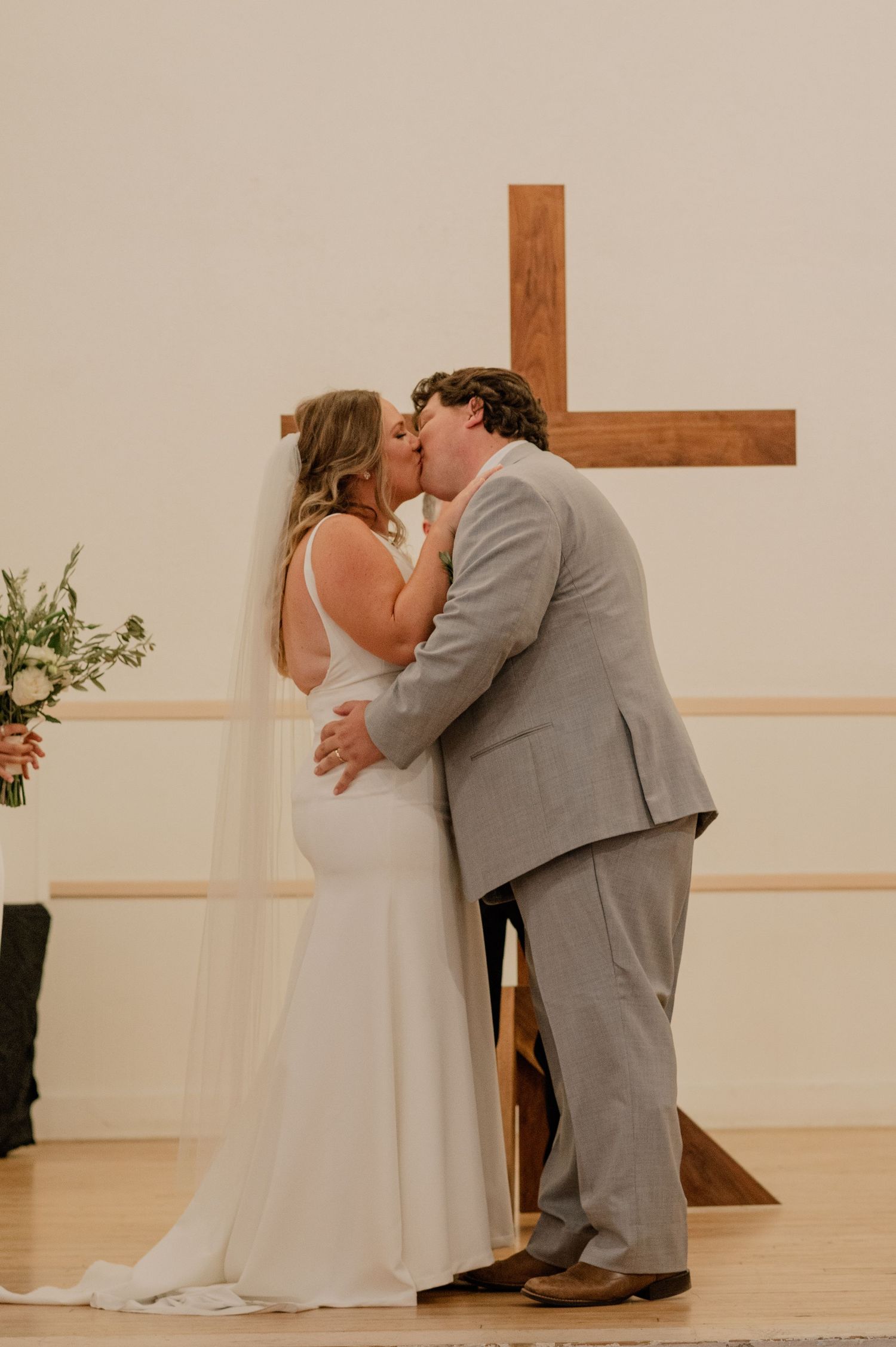 Newlyweds share their first kiss as a married couple in front of a wooden cross.