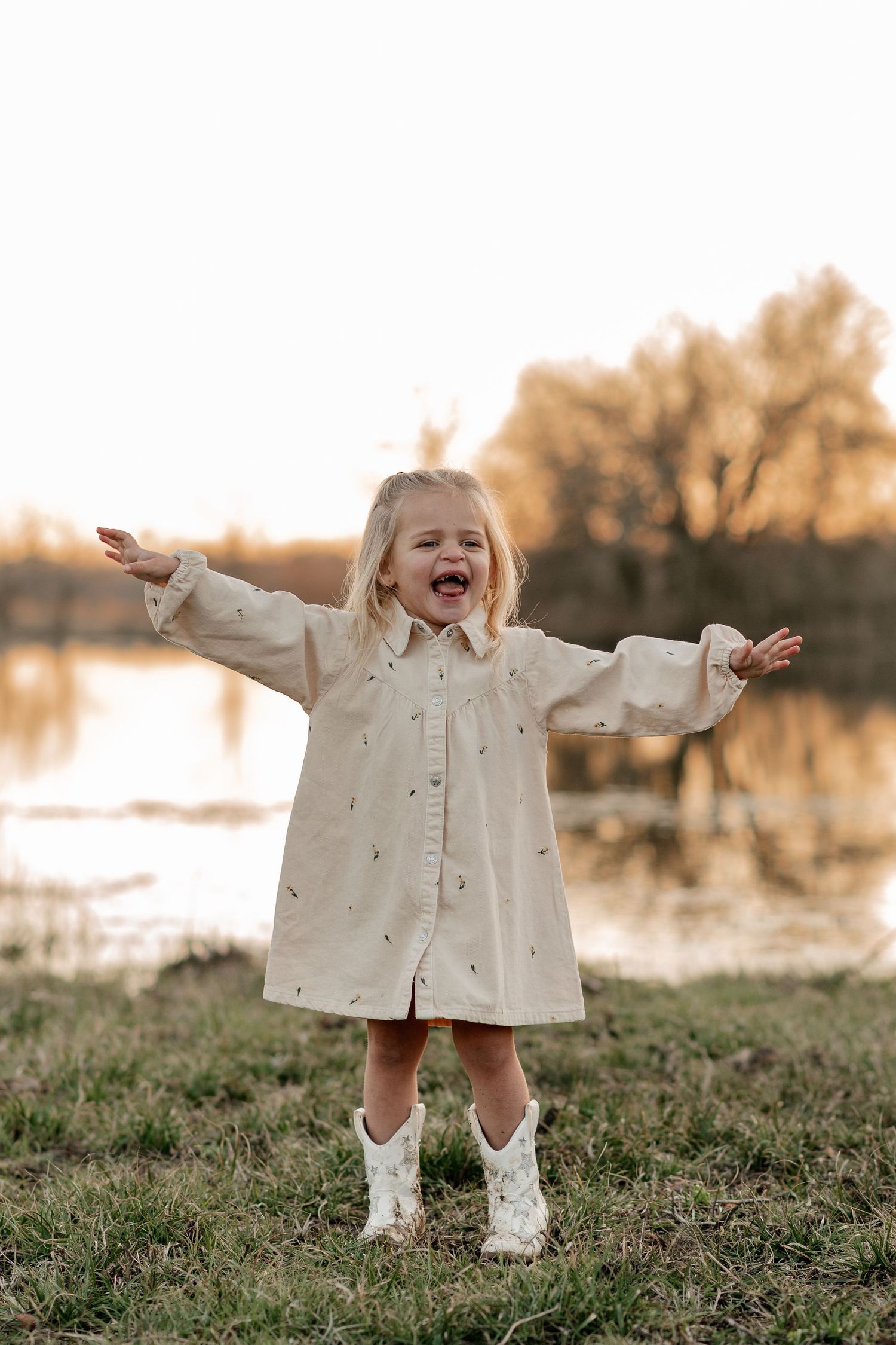 Candid photo of a joyful young girl at an at-home family session in front of a large pond on their farm in Greenville, TX