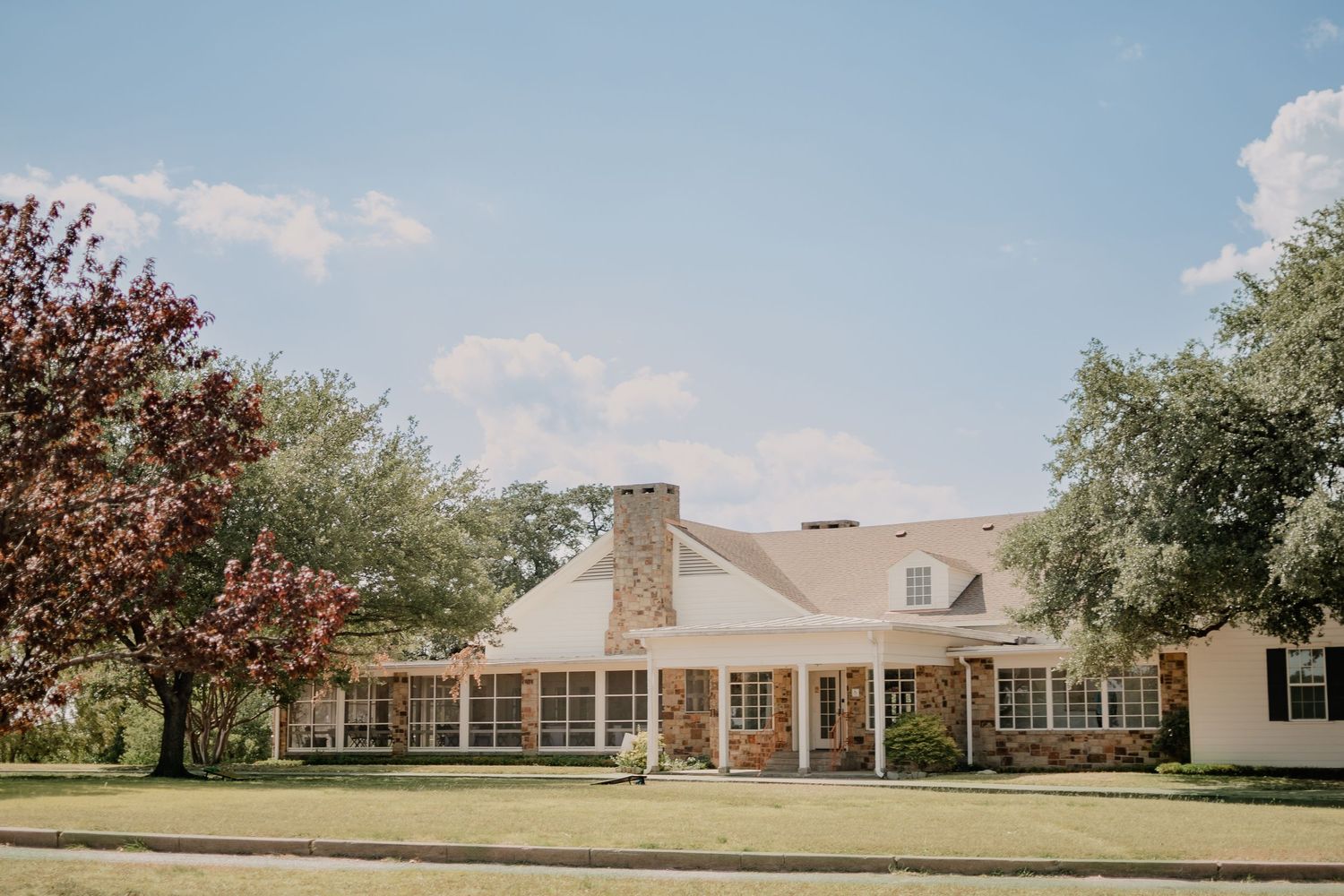 Large white ranch-style venue with brick facade and symmetrical windows on a sunny day.