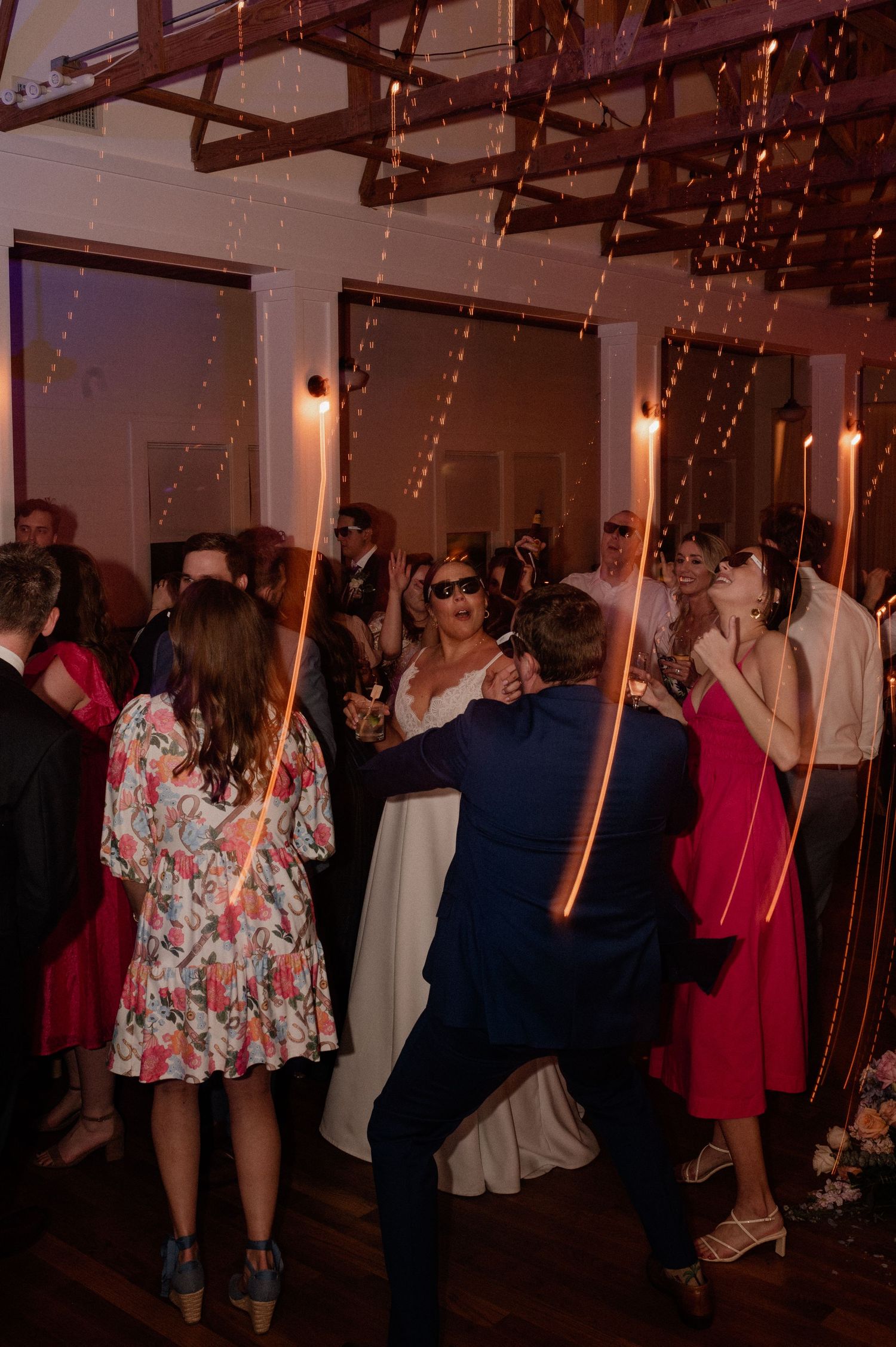 Wedding reception dance floor filled with guests under decorative lighting.