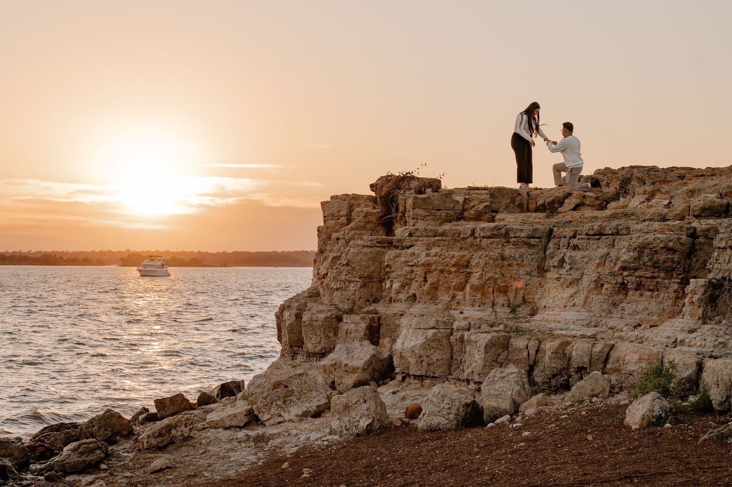 Wide shot of man proposing on a rock cliff overlooking the lake at sunset at Rockledge Park in Grapevine, Texas for a couples photo session