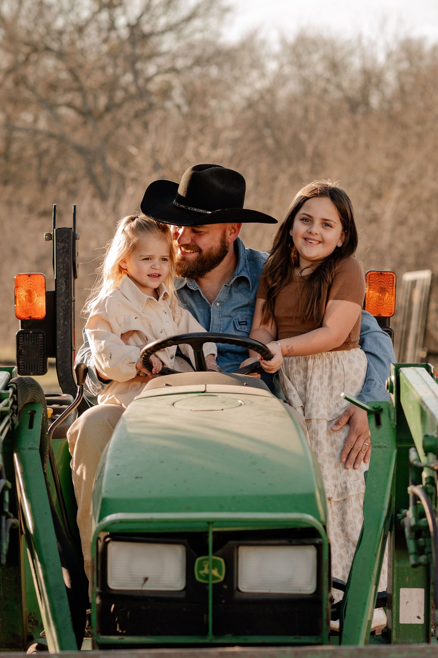 Candid lifestyle photo of 2 girls in a tractor with their dad out in the country for an at-home family session in Greenville, Texas