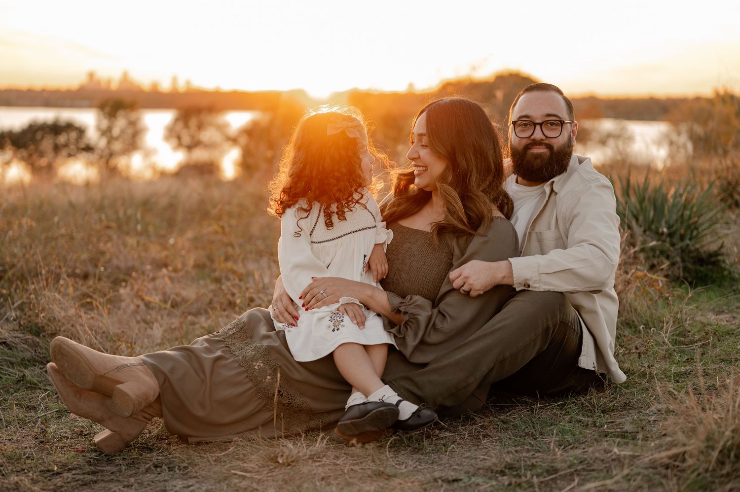 Candid photo of family cuddled up in the tall grass of a field overlooking the White Rock Lake in East Dallas, Texas