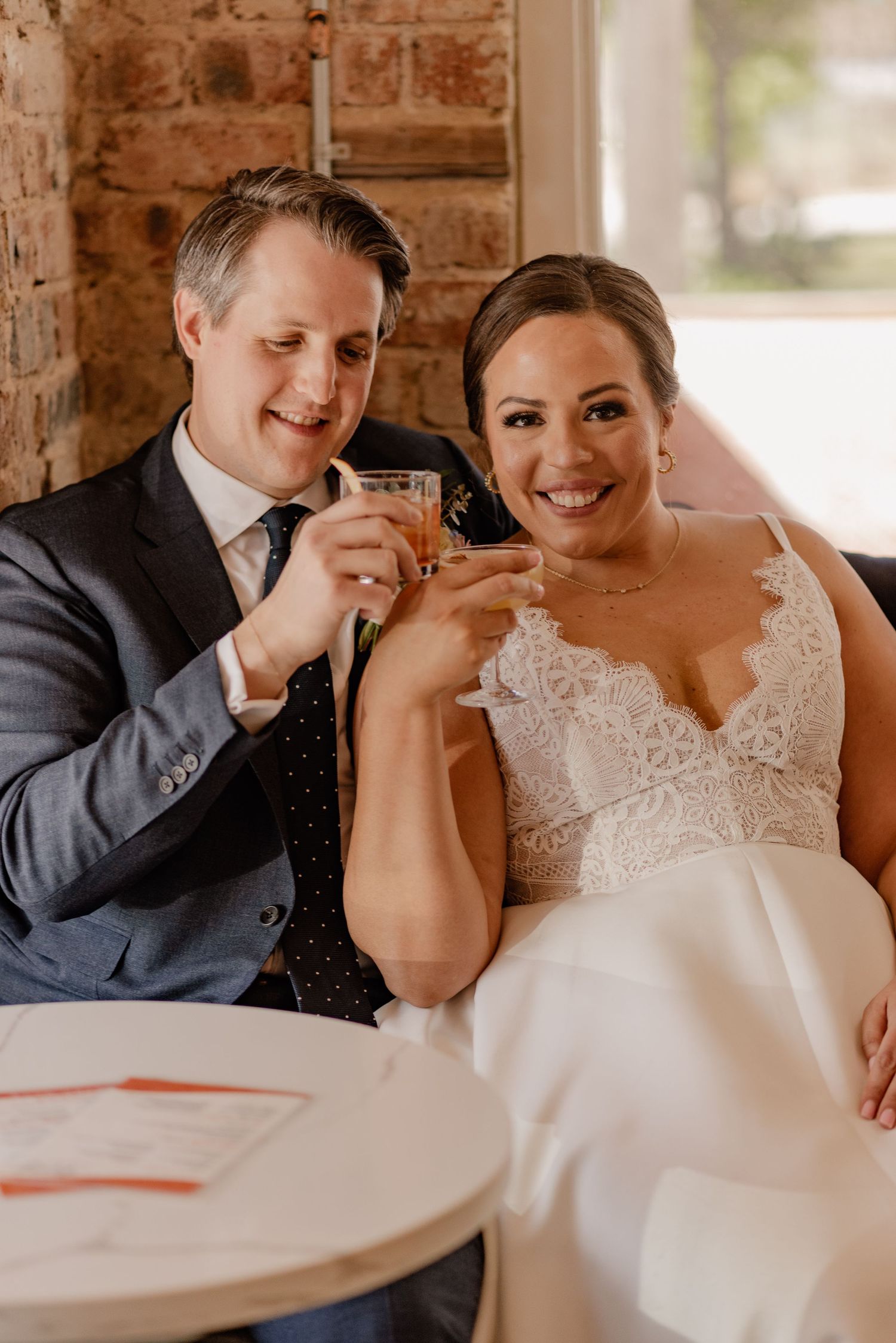 Wedding couple toasts with cocktails while relaxing at cafe table in Bishop Arts bar in Dallas, TX