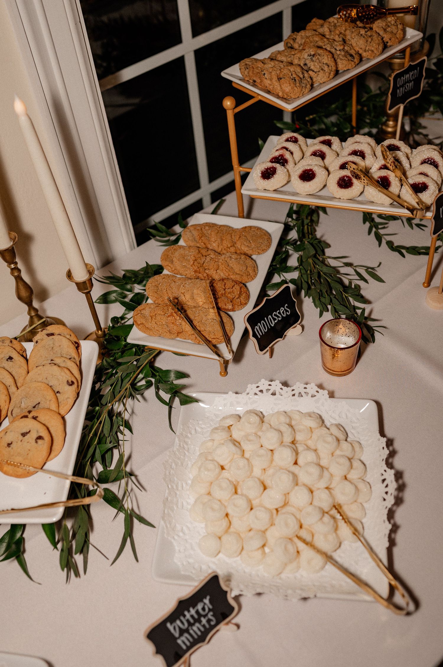 Flash photo of an elegant wedding dessert table with mints, cookies, and greenery on white platters