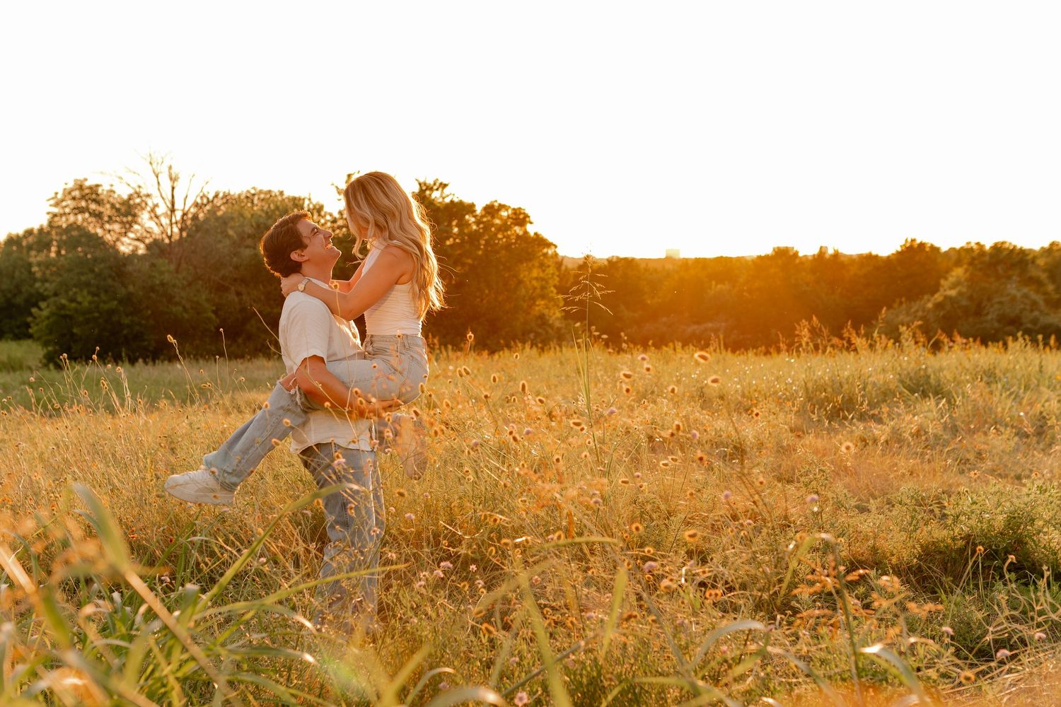 Couple sharing a romantic moment in a golden sunlit field, man lifting woman joyfully at sunset in Dallas, Texas