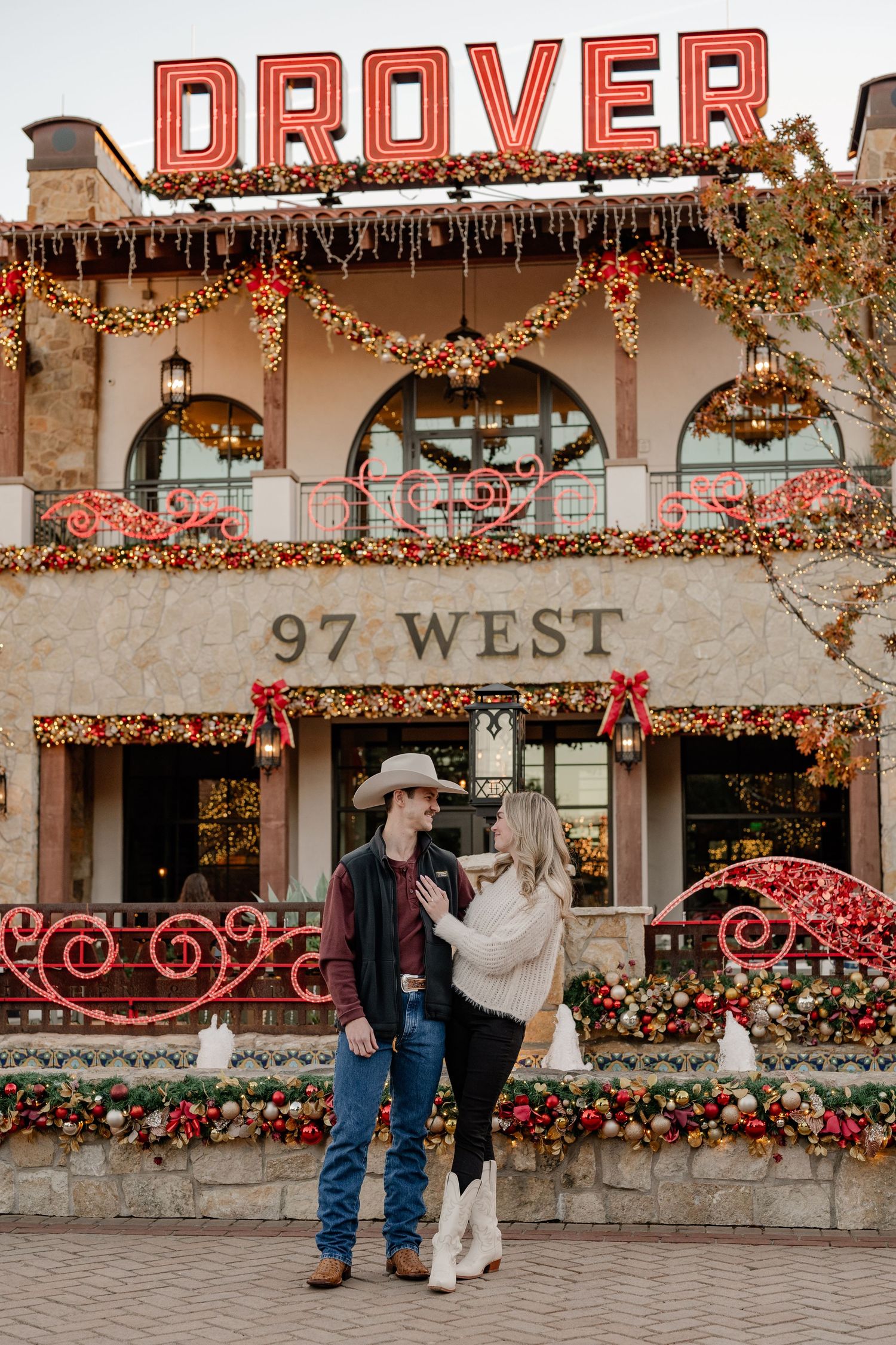 Recently engaged couple posing while hugging in front of Dover hotel in Ft Worth, Texas at Christmas time
