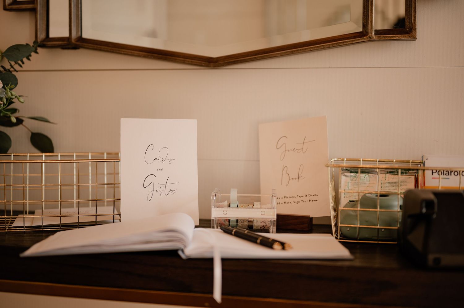 Wedding signage and decor arranged on a white table with gold wire baskets.