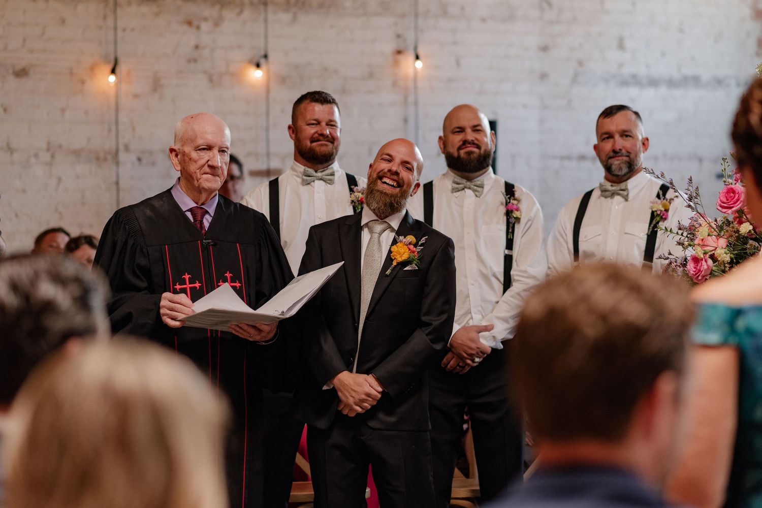 Joyful candid close-up of Groom in front his groomsmen seeing his Bride down the aisle in an indoor Summer wedding ceremony in Dallas, Texas
