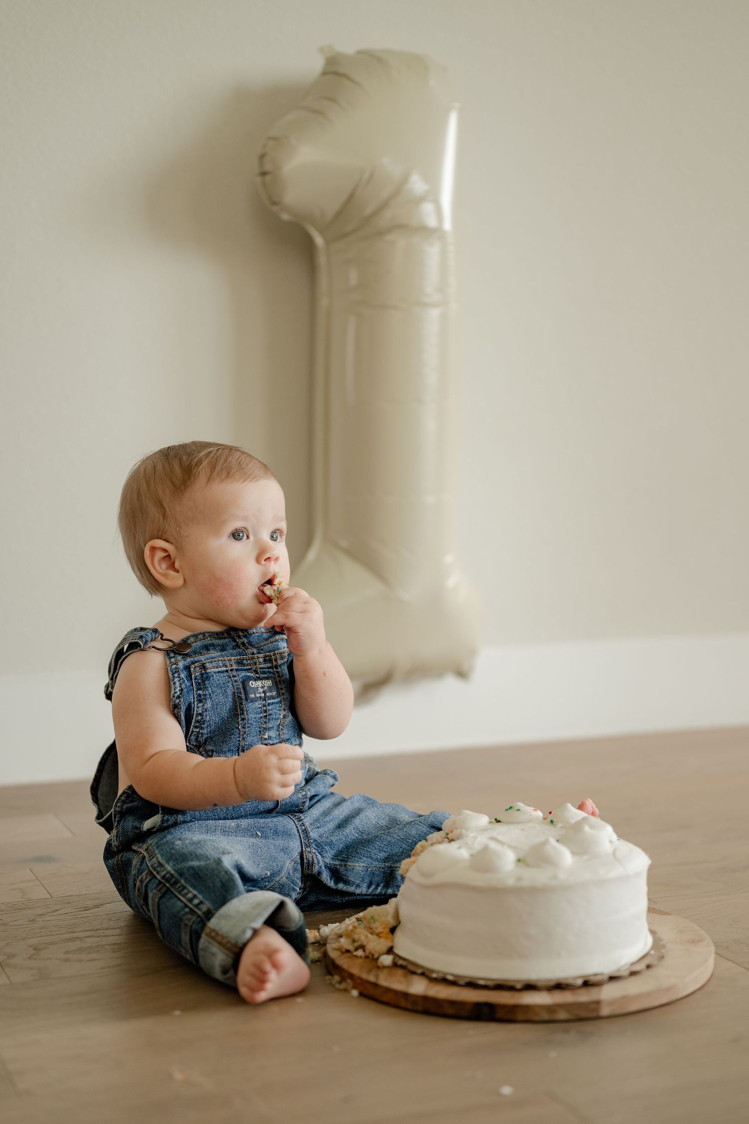 One year old in overalls eating cake in front of a 