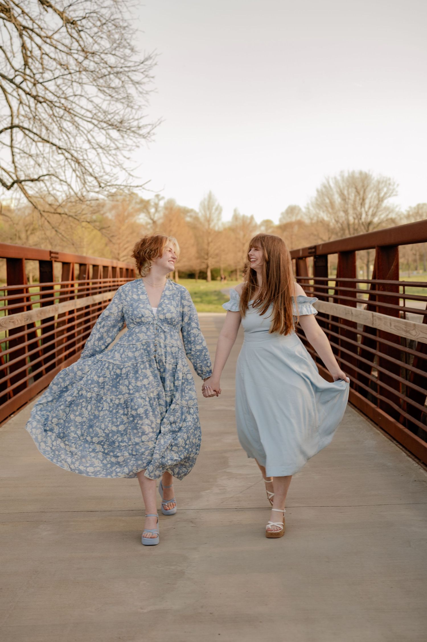 Two sister prancing across a metal industrial bridge in long flowy blue dresses during a fall family photo session