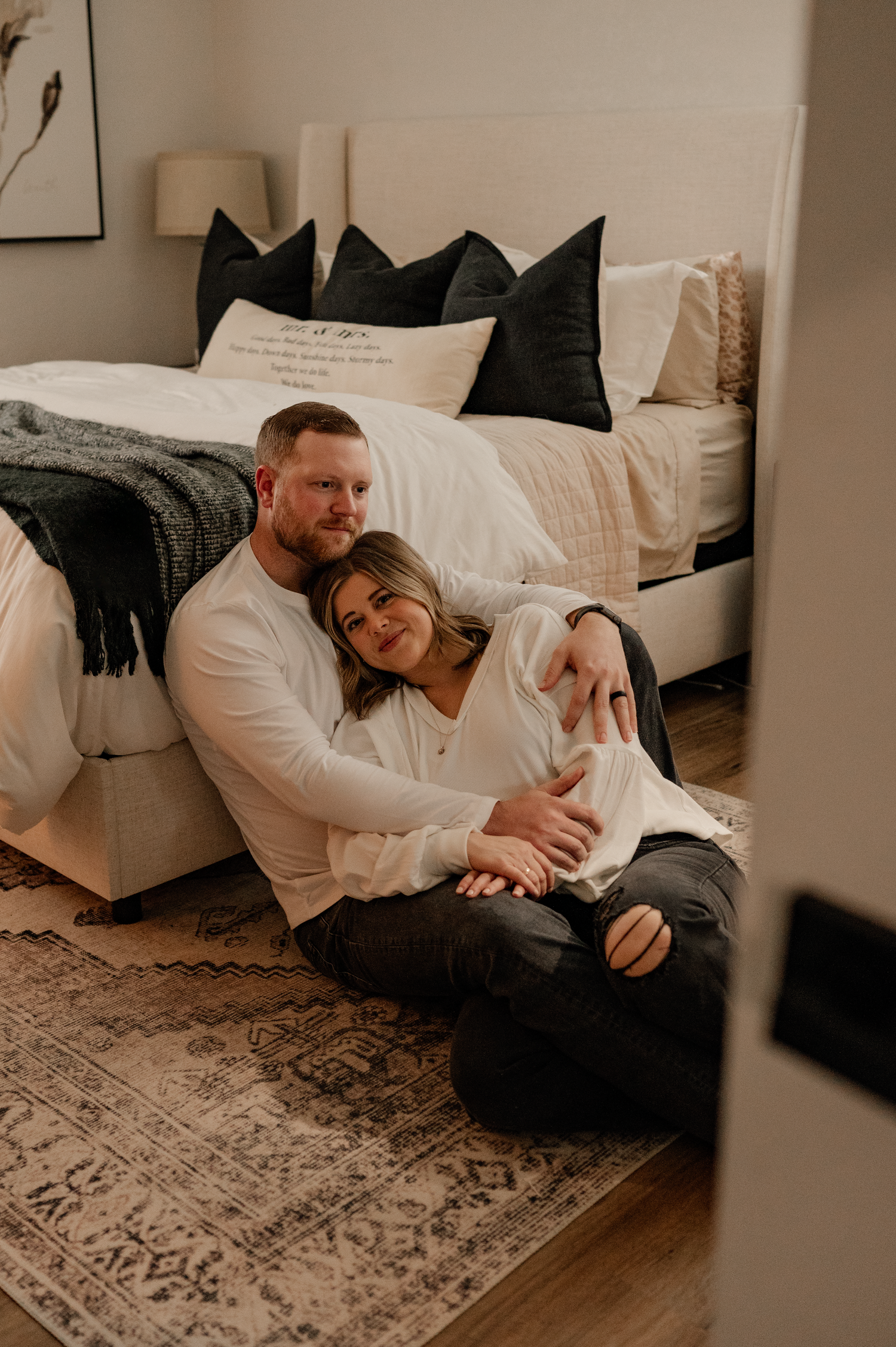 Couple lounging on floor with white sofa and patterned rug in background.