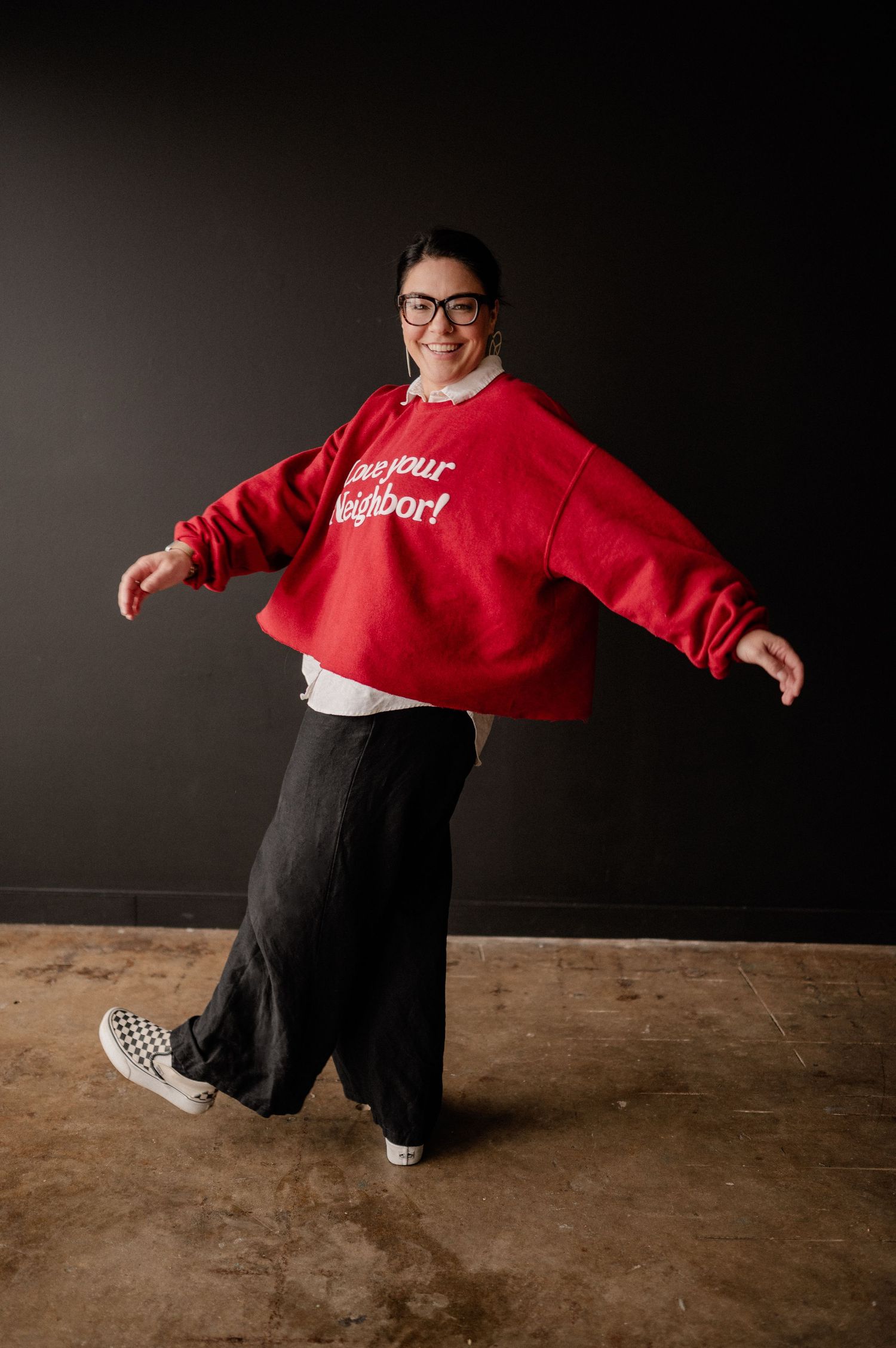 Playful branding headshot of a female photographer in a bright sweater in front of a black wall at a studio in Richardson, Texas