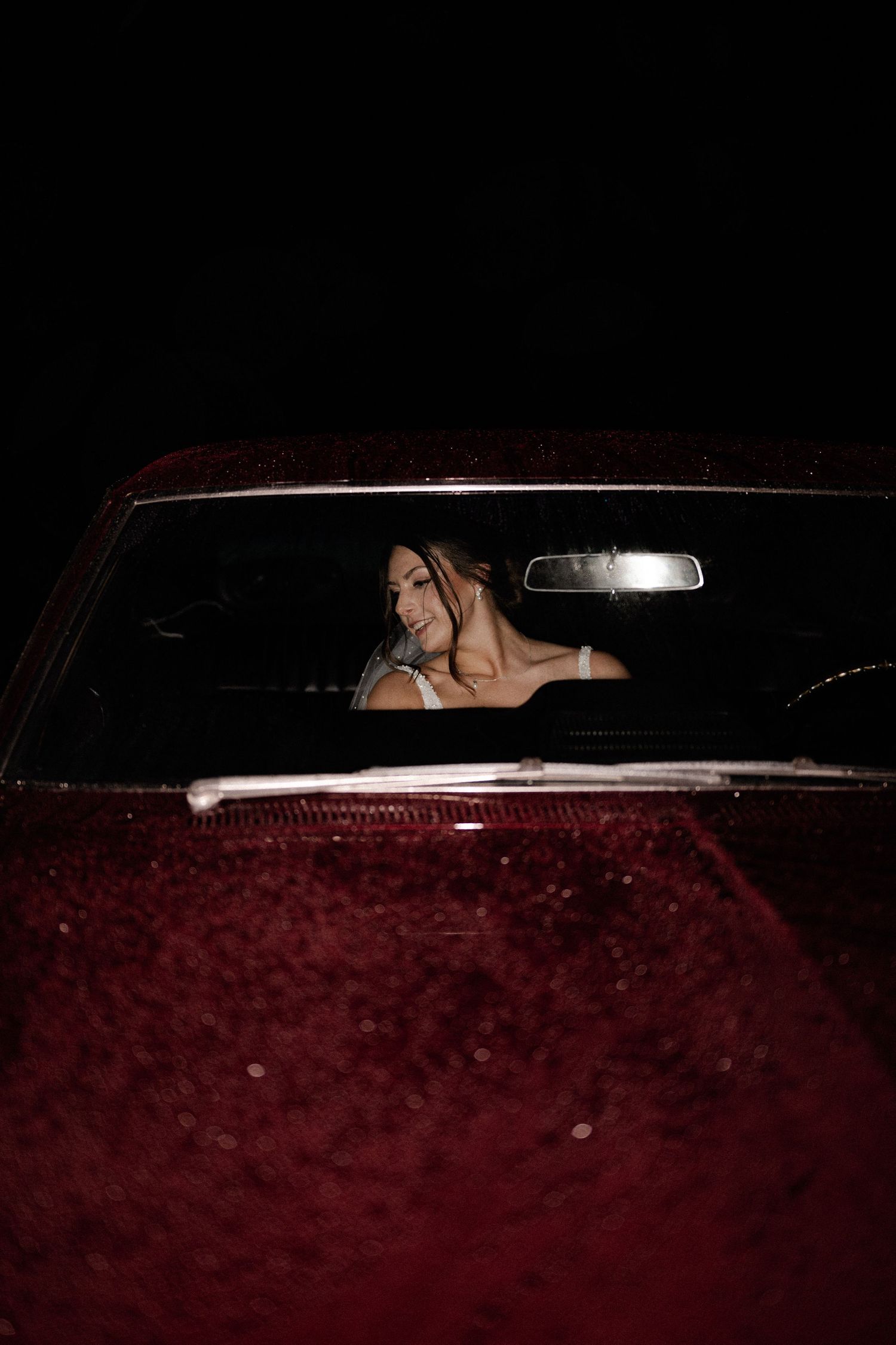 Moody image of a bride sliding into a vintage care after the wedding grand exit